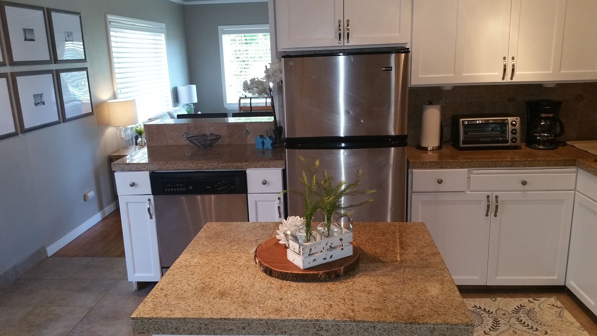 Modern kitchen with white cabinets, stainless fridge, granite island, and a plant centerpiece