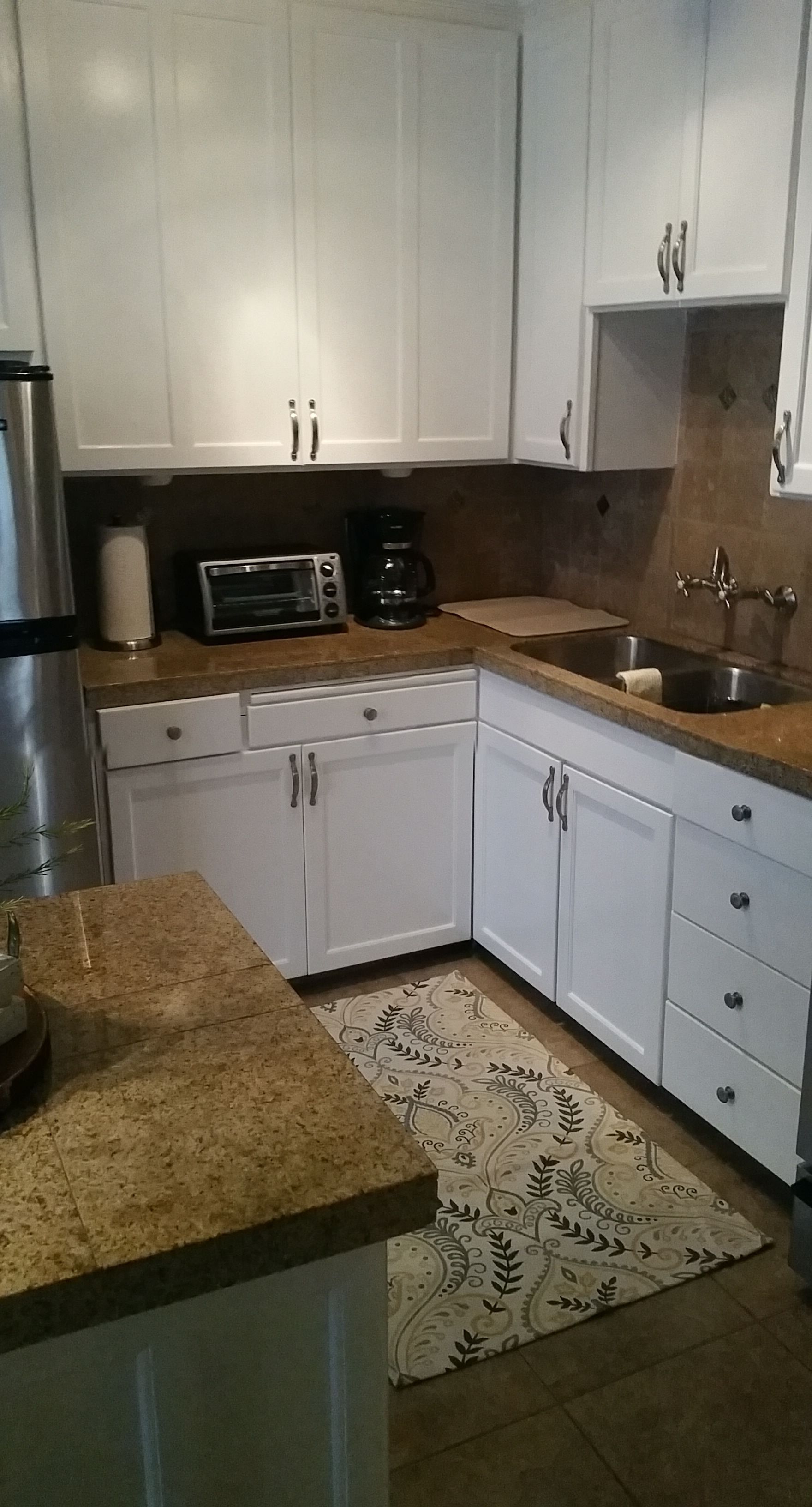 Small kitchen with white cabinets, wood countertops, sink, toaster oven, coffee maker, and patterned rug.