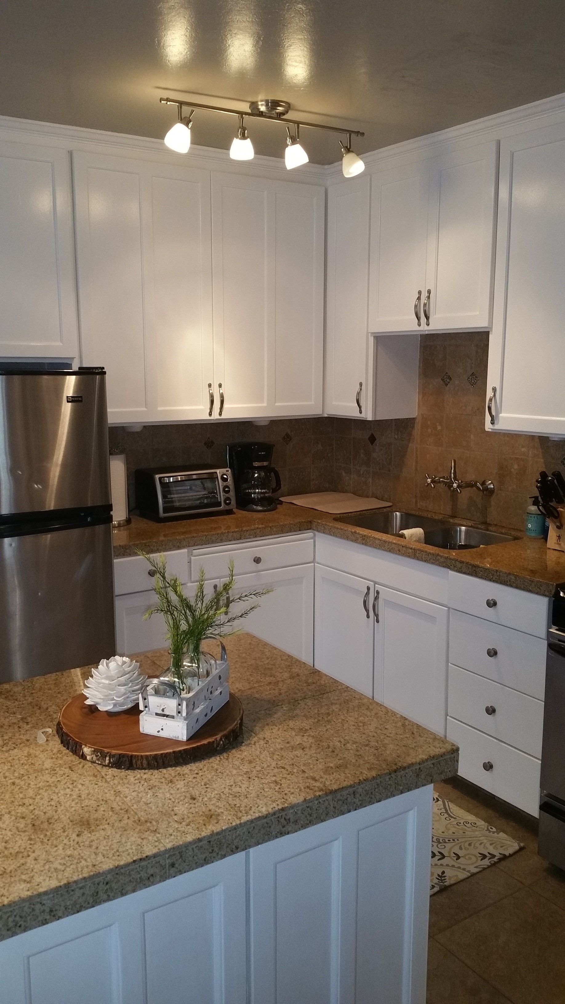 Bright kitchen with white cabinets, stainless fridge, granite counters, and a central island.