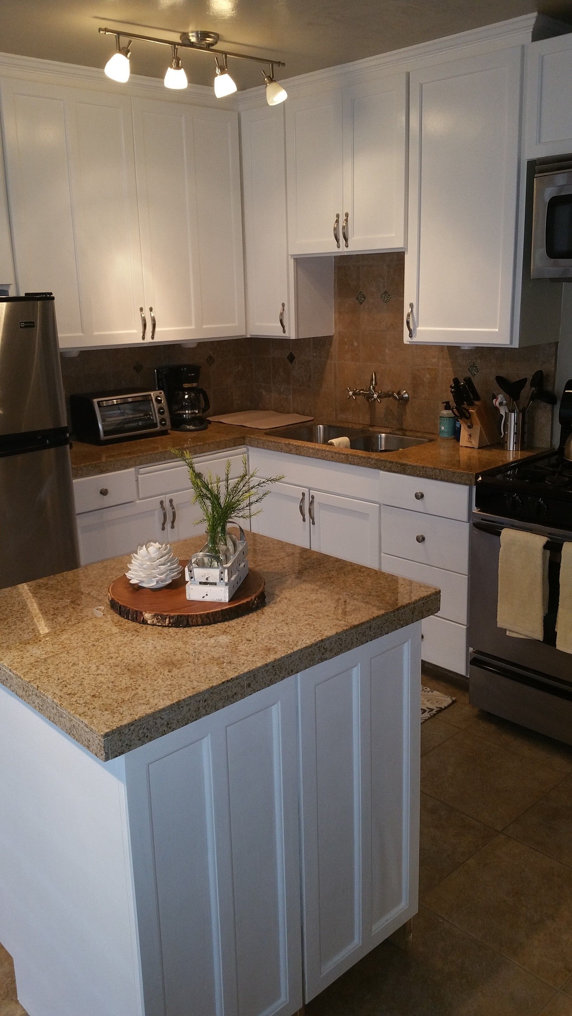 Modern kitchen with white cabinets, stainless appliances, and a granite island with a small plant centerpiece