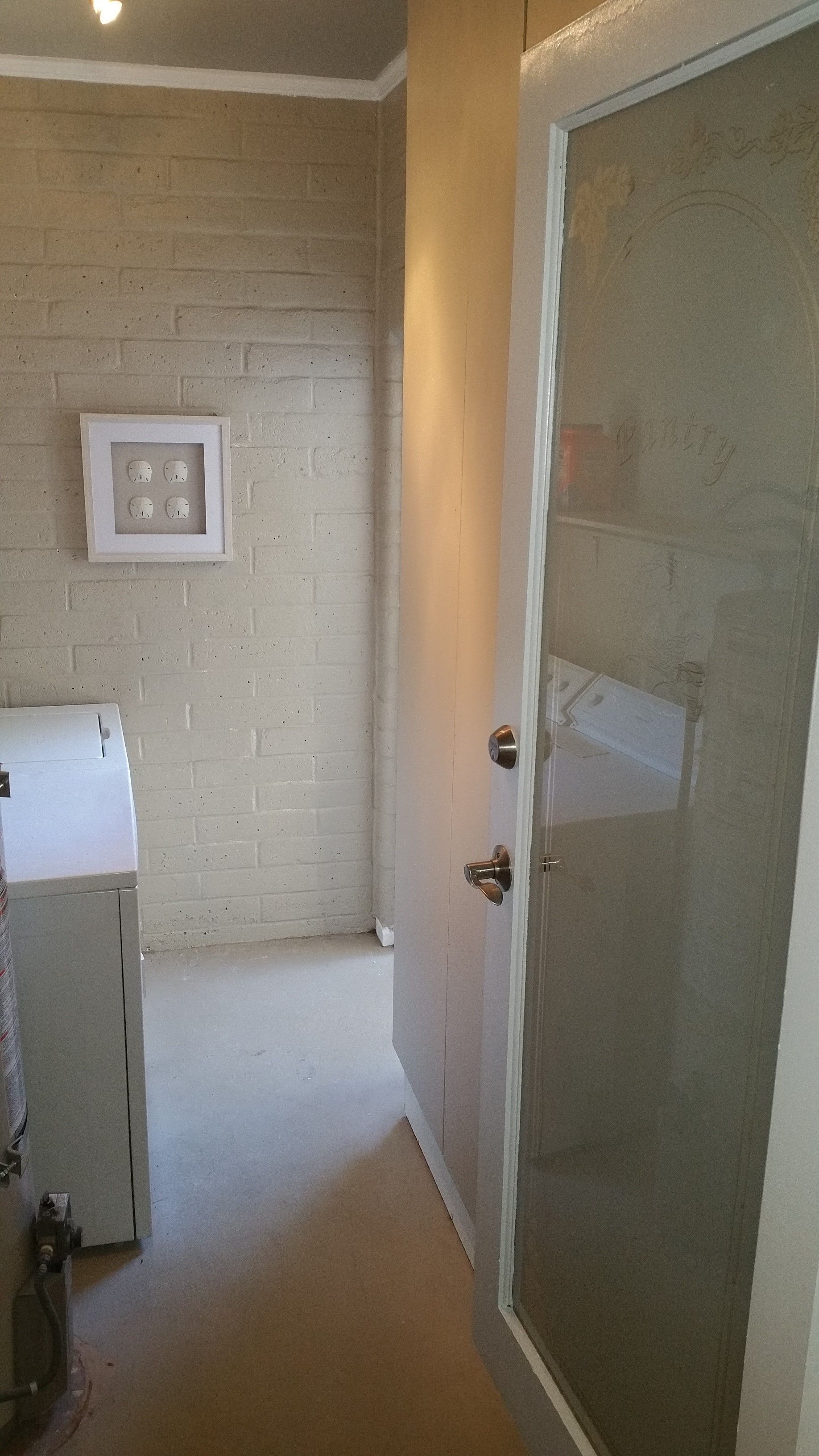 Open door into a small, beige hallway with framed wall art and a frosted glass panel.