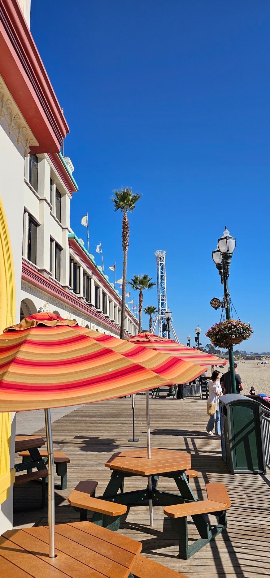 Outdoor café patio with striped umbrellas, tables, and lampposts along a sunny waterfront promenade