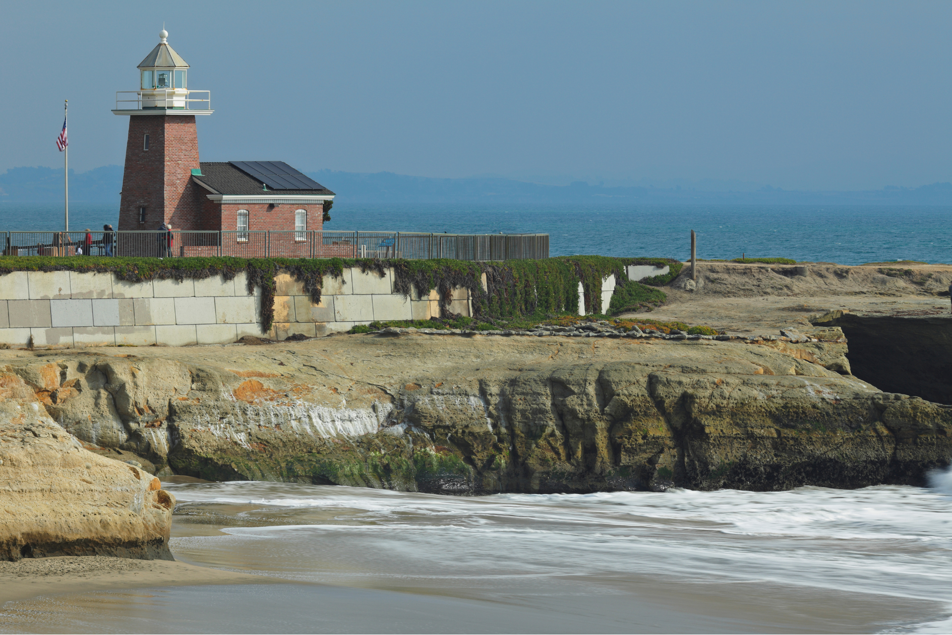 Lighthouse on a rocky seaside cliff with waves and blue ocean in the background