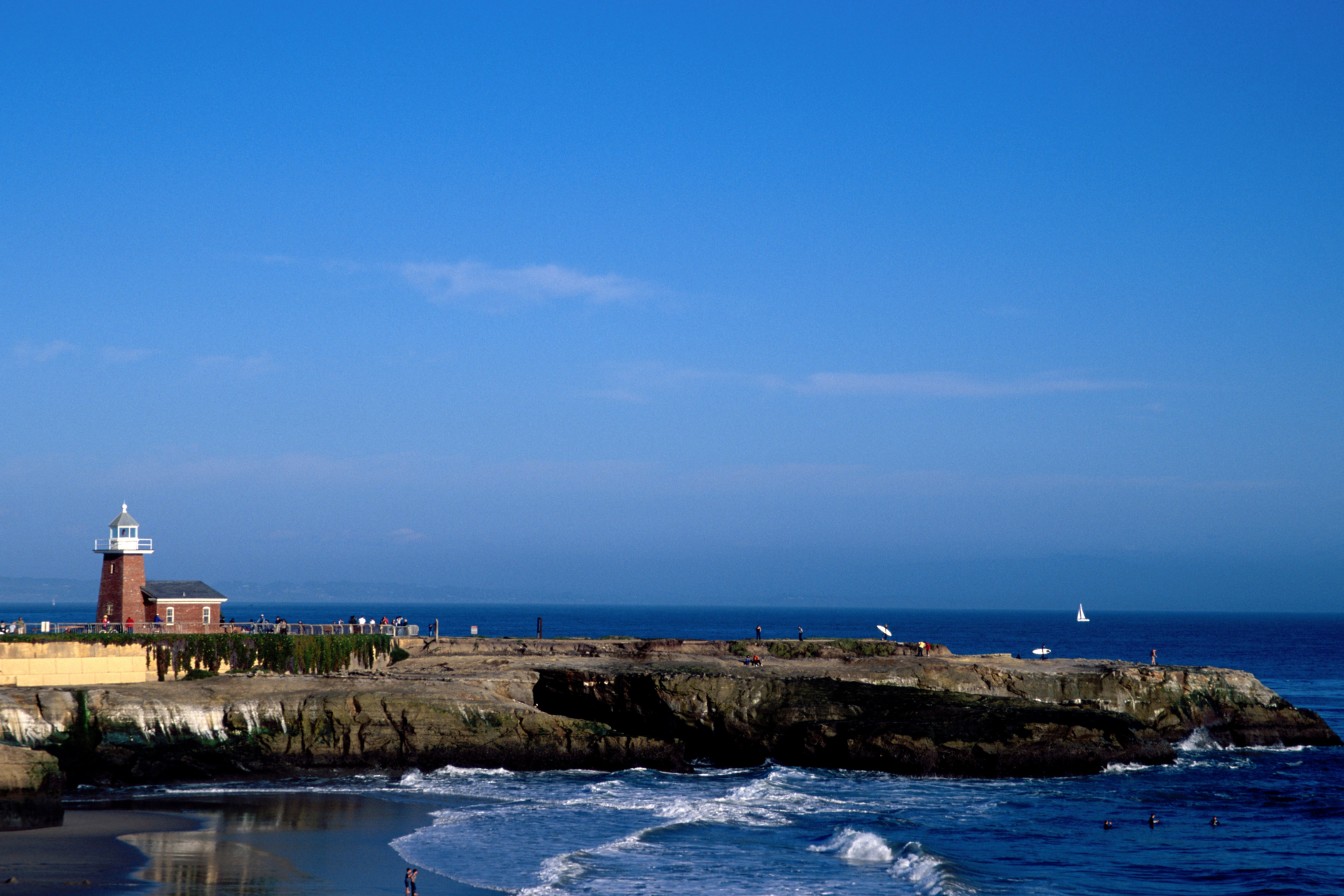 Lighthouse on a rocky coastline with waves under a clear blue sky