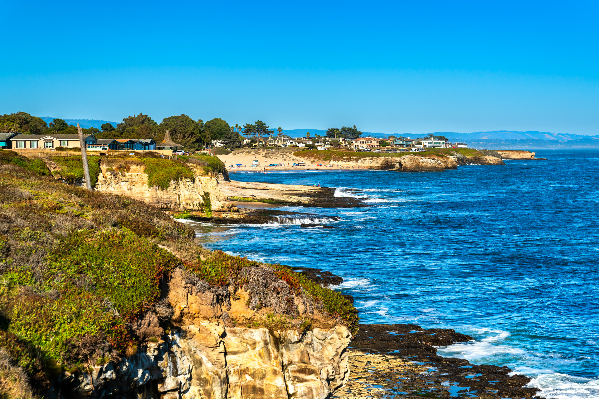 Rocky coastline with blue ocean, cliffs, and a sunny shoreline under a clear sky