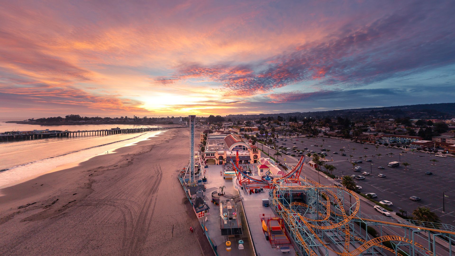 Sunset over a beach boardwalk with colorful lights and a fairground by the shoreline