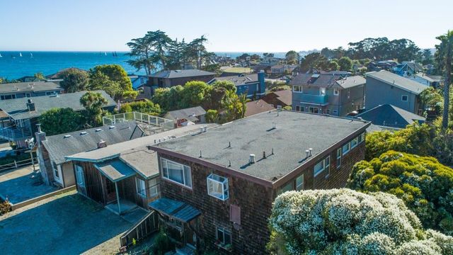 Aerial view of a coastal neighborhood with a brick building, trees, and ocean in the background