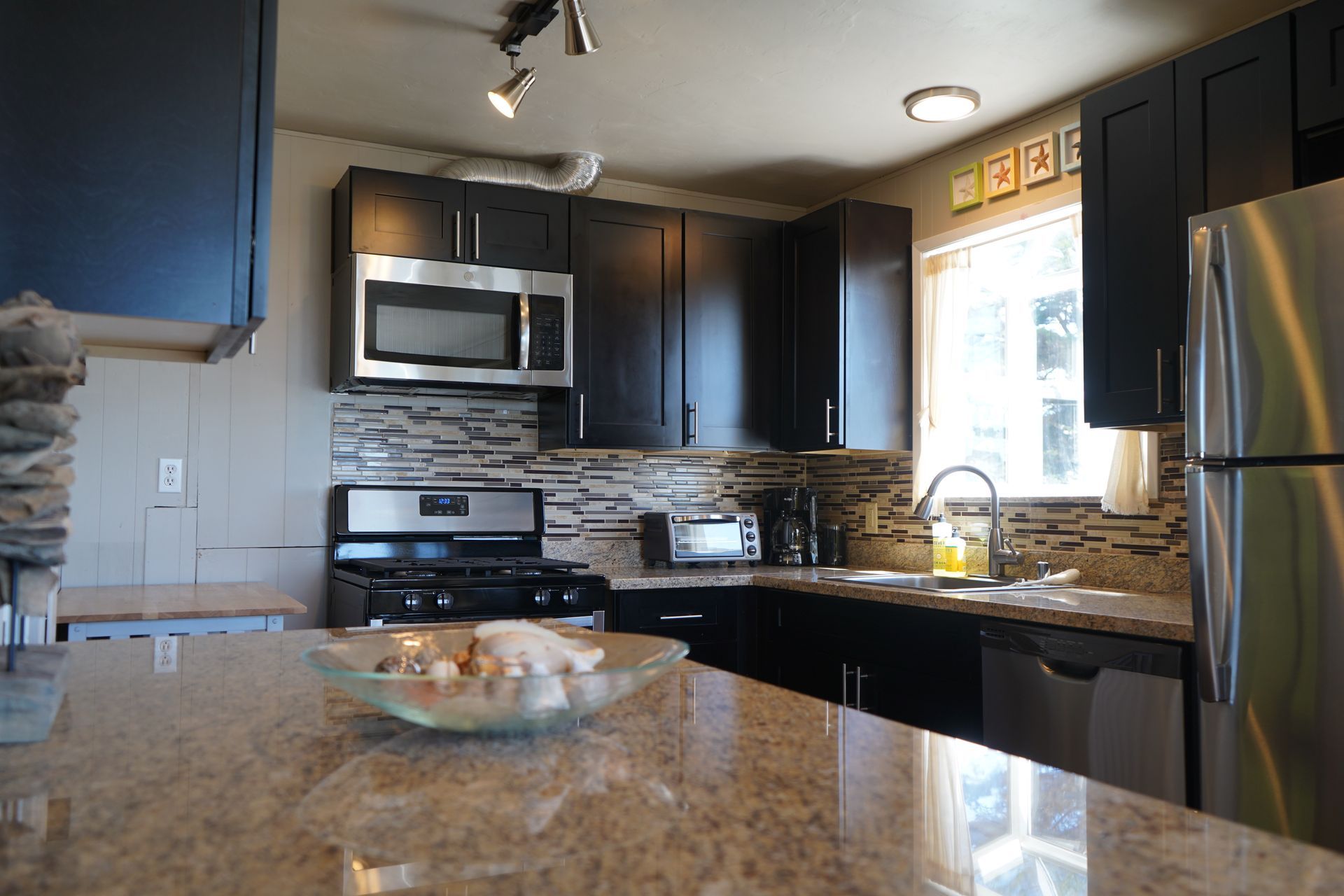 Modern kitchen with dark cabinets, stainless appliances, granite counters, and a bowl of fruit on the island