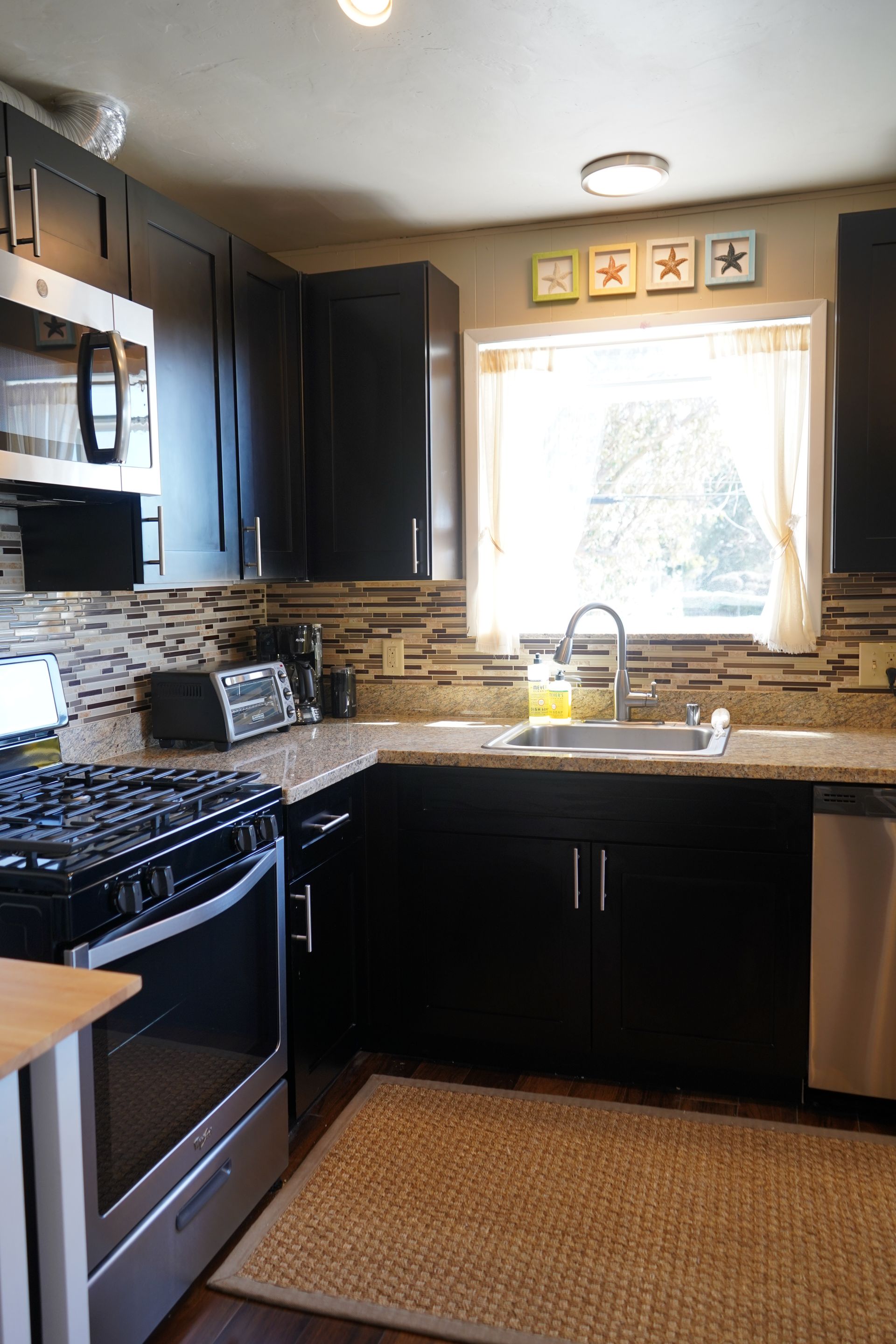 Compact kitchen with dark cabinets, stainless stove, tiled backsplash, and a sunlit window over the sink.
