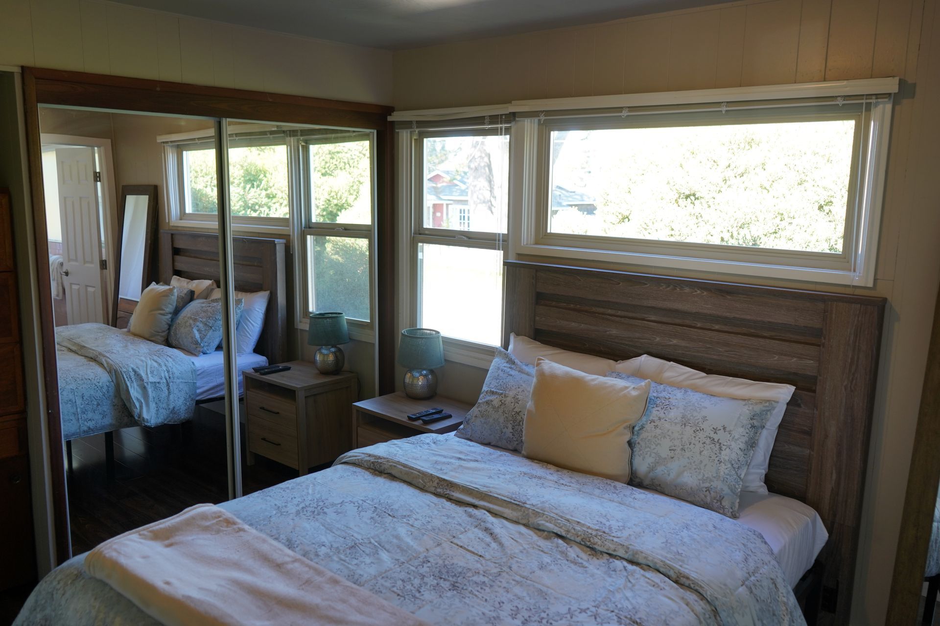 Bedroom with bed, mirrored closet, and large windows letting in daylight