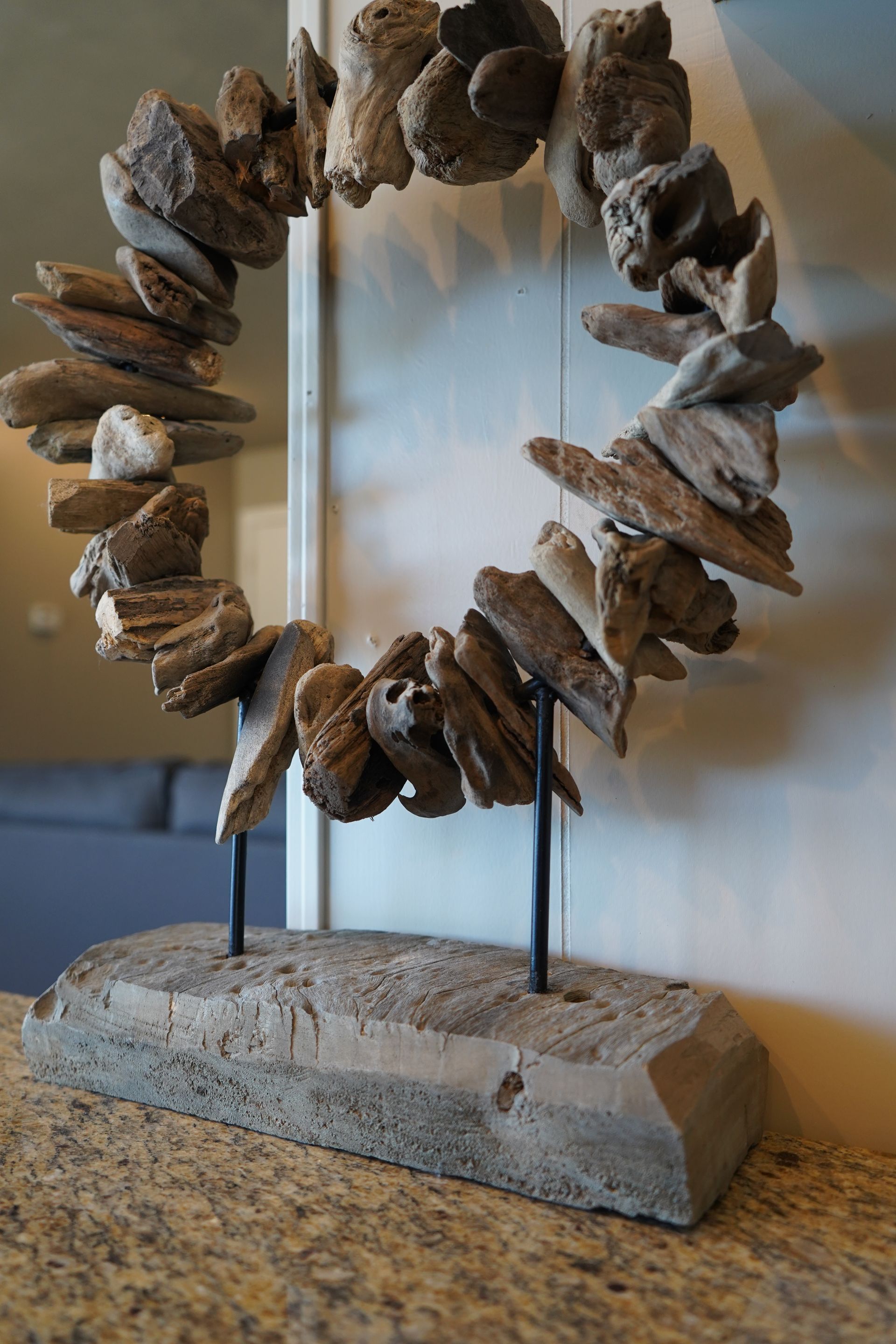 Rock sculpture shaped like a ring on a stone base, displayed indoors against a wall.