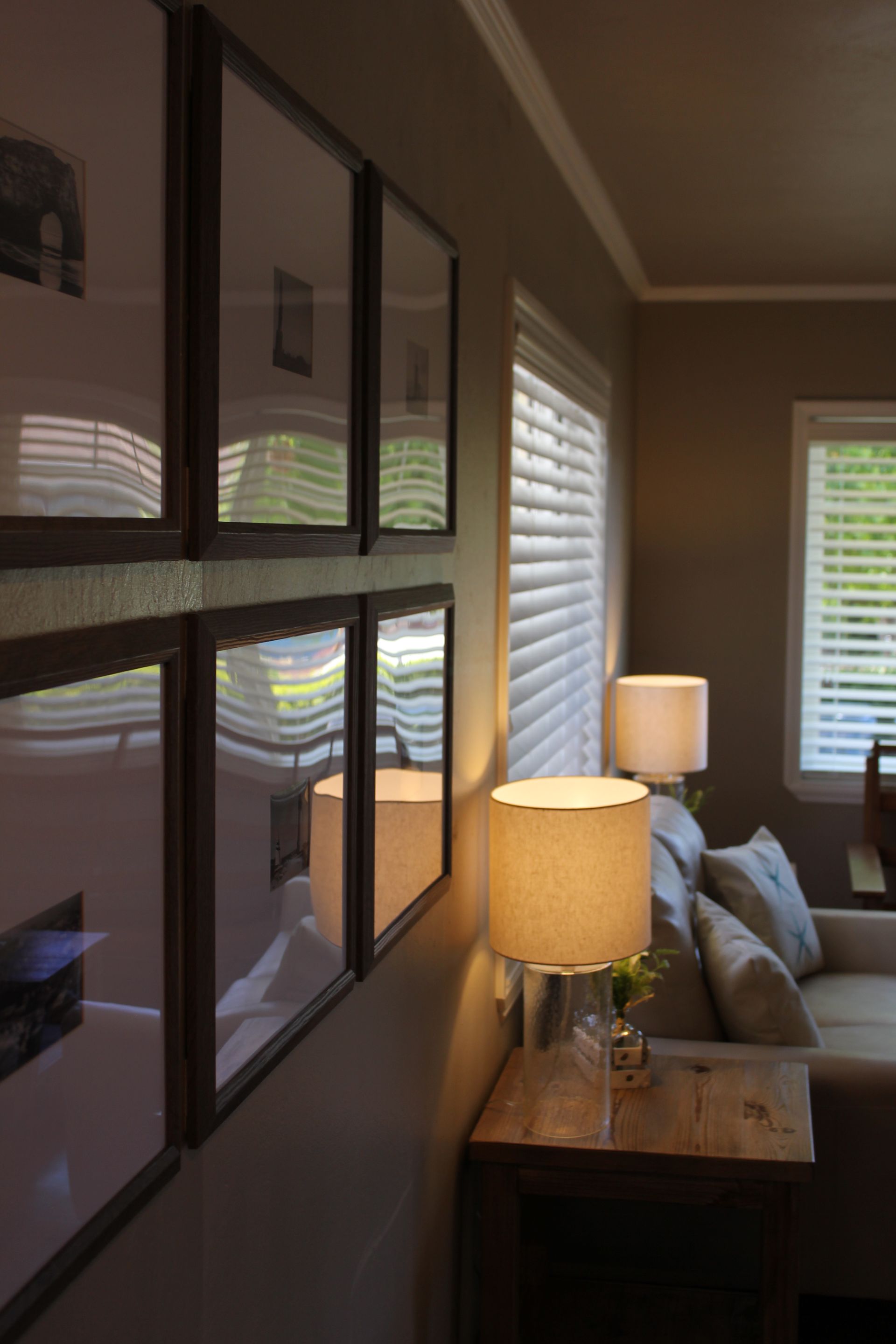 Living room hallway with framed wall art, lit table lamps, couch, and white shutters