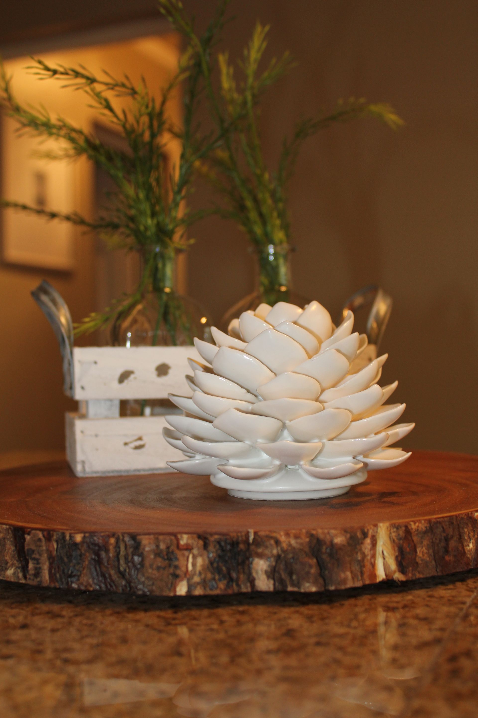 White decorative flower on a rustic wooden slab with a small candle holder and greenery in the background