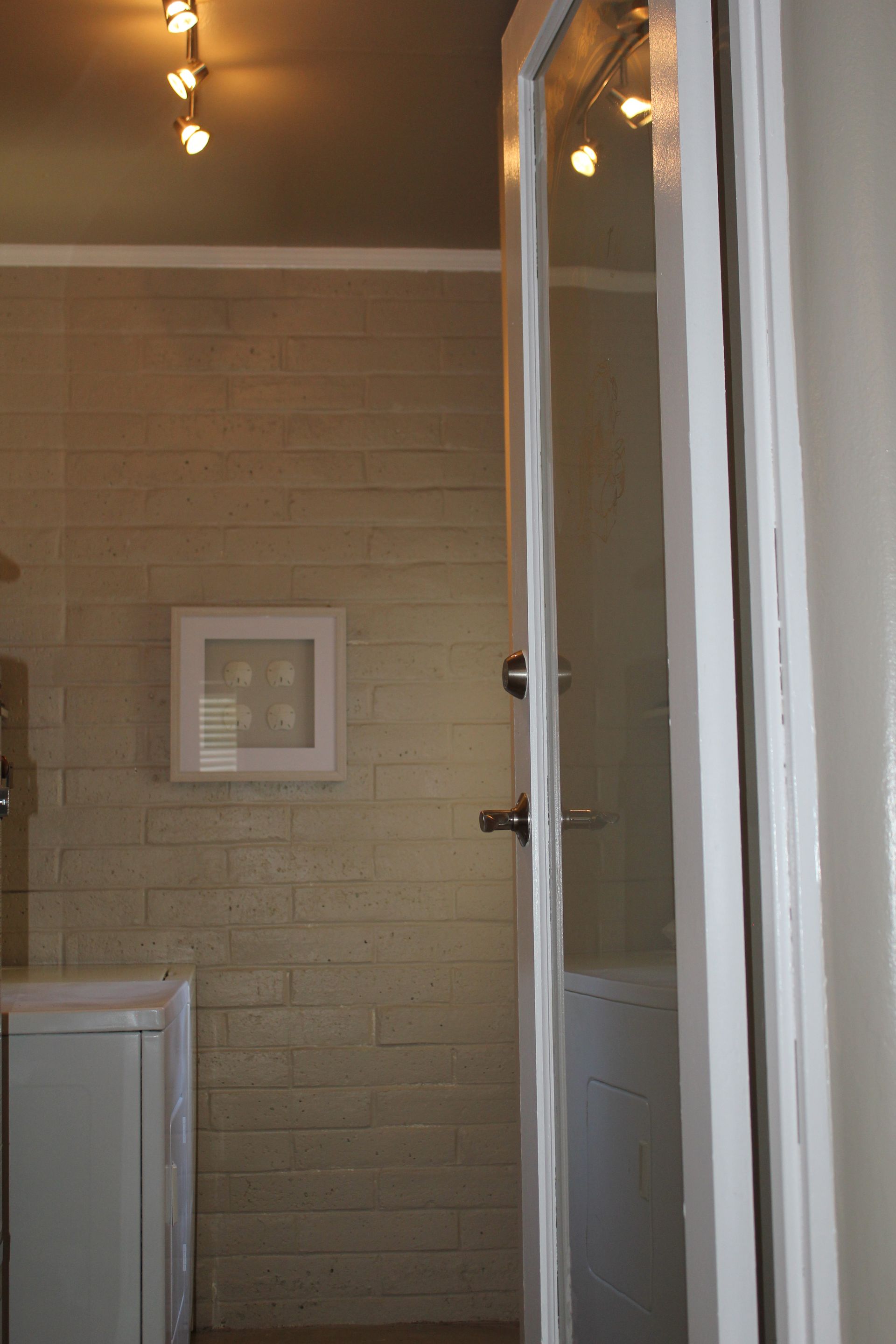Indoor bathroom with beige tiled wall, framed picture, and glass shower door partially open