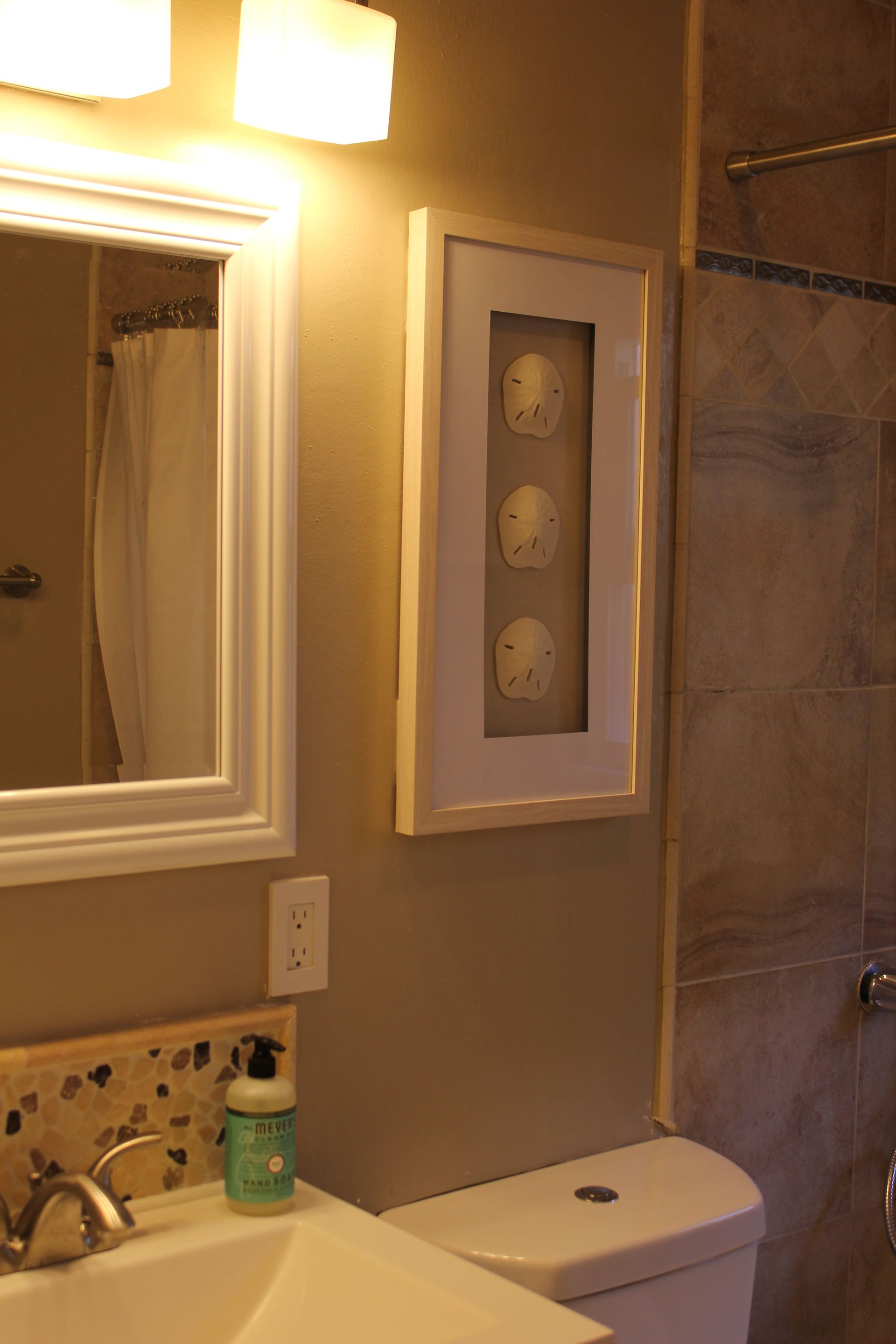 Bathroom vanity with mirror, sink, toilet, and framed wall art in warm lighting