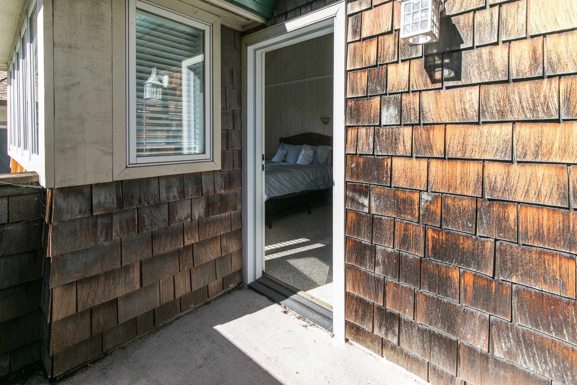Front porch entry with open door, window, shingle siding, and sunlight on the ground