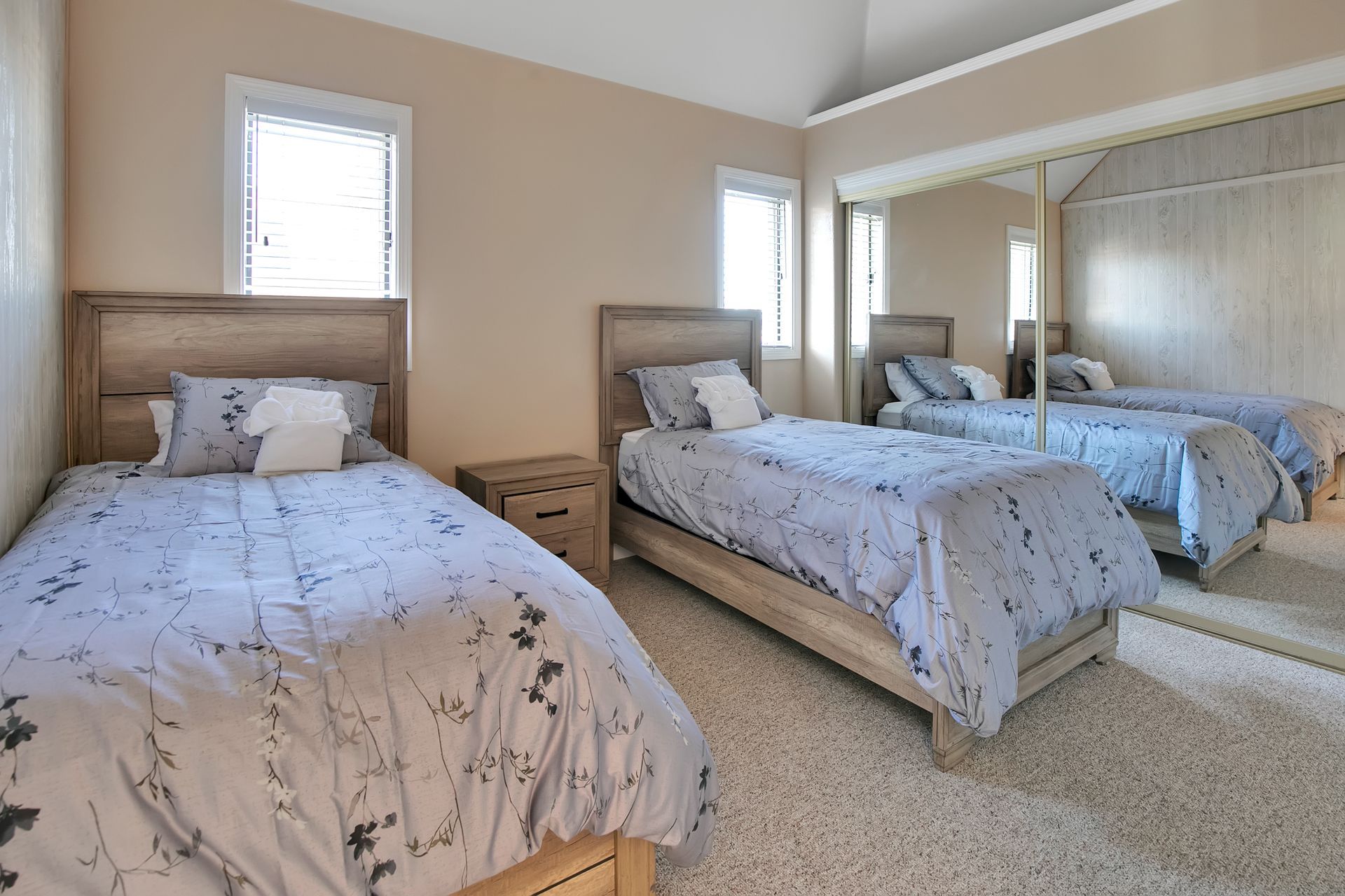 Bright bedroom with two twin beds, pale blue floral bedding, mirrored closet, and carpeted floor