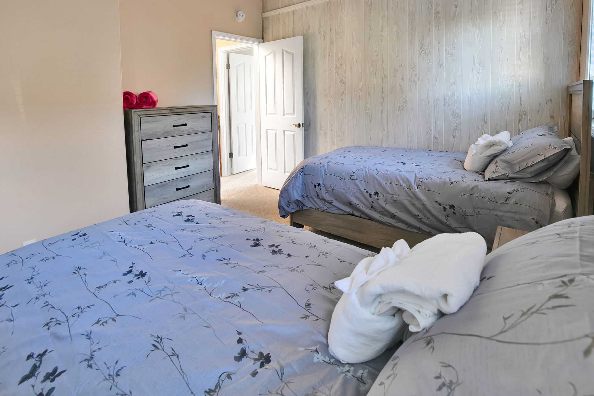 Bedroom with two beds, a dresser, and an open door, in soft neutral tones.