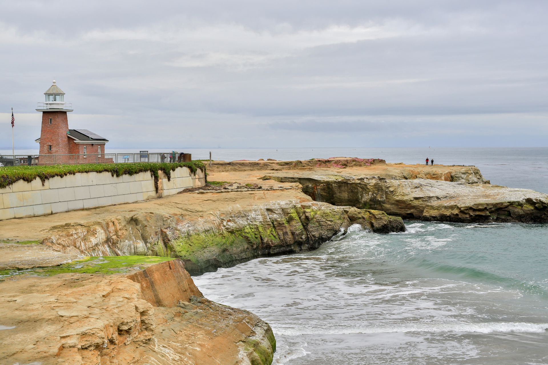 Coastal lighthouse on a rocky cliff beside rough ocean waves under a cloudy sky