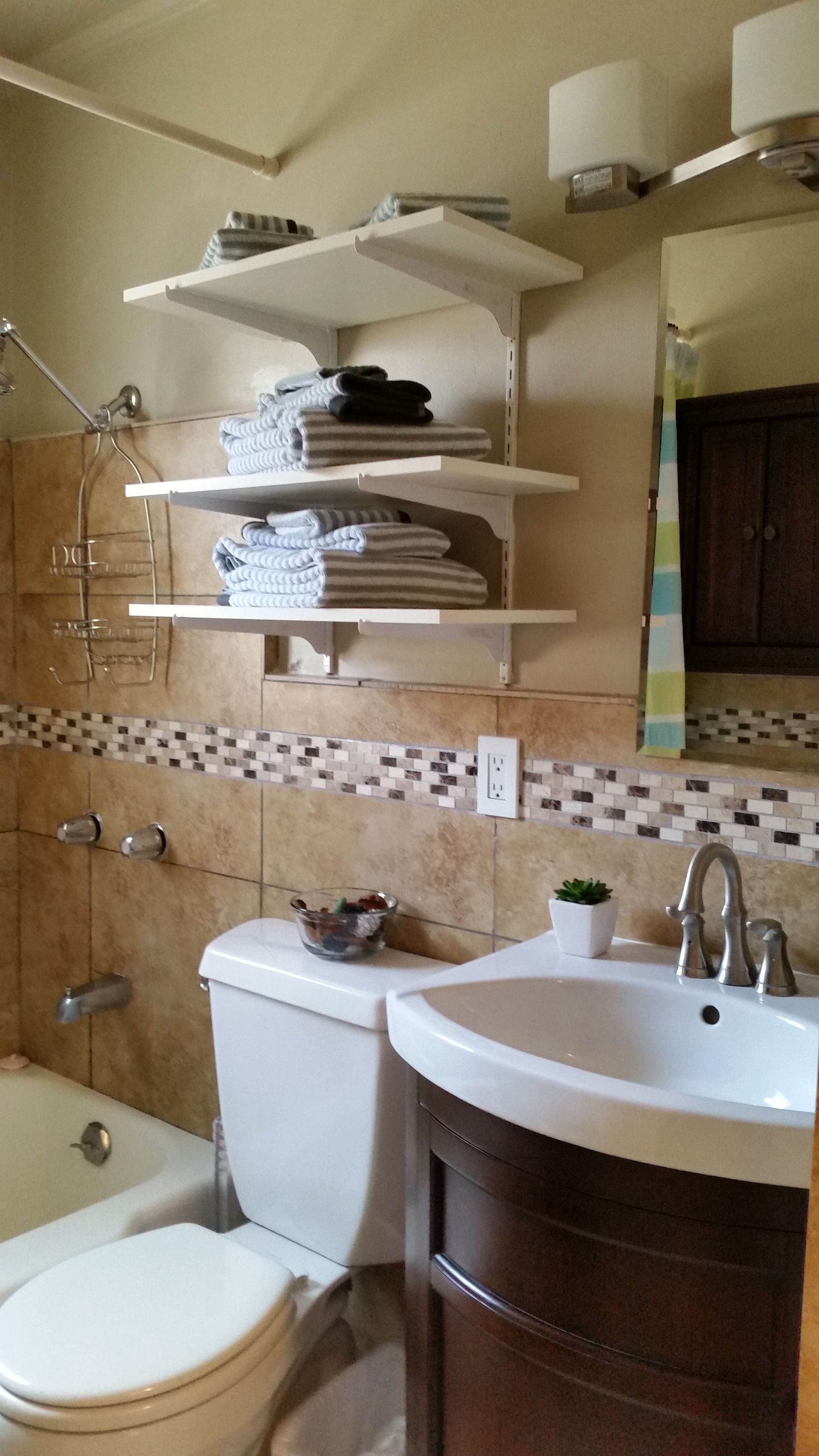 Small bathroom with tub, toilet, sink, mirrored cabinet, and wall shelves holding towels and toiletries.