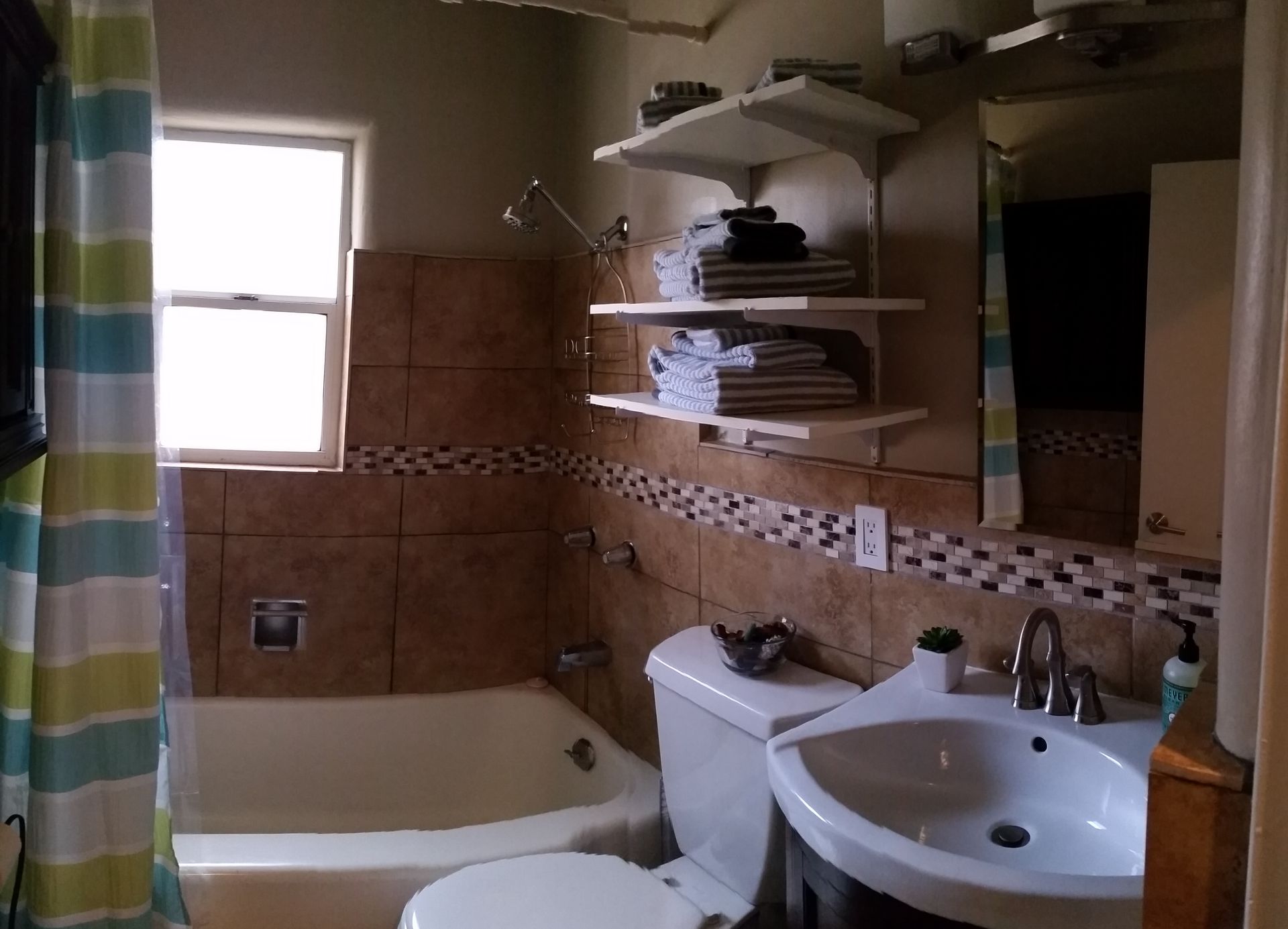 Bathroom with tub, toilet, sink, tan tile walls, and a striped shower curtain