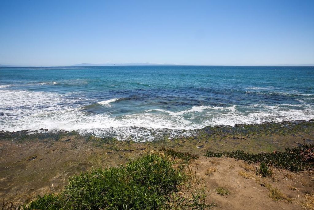 Rocky shoreline with green vegetation and a calm blue ocean under a clear sky