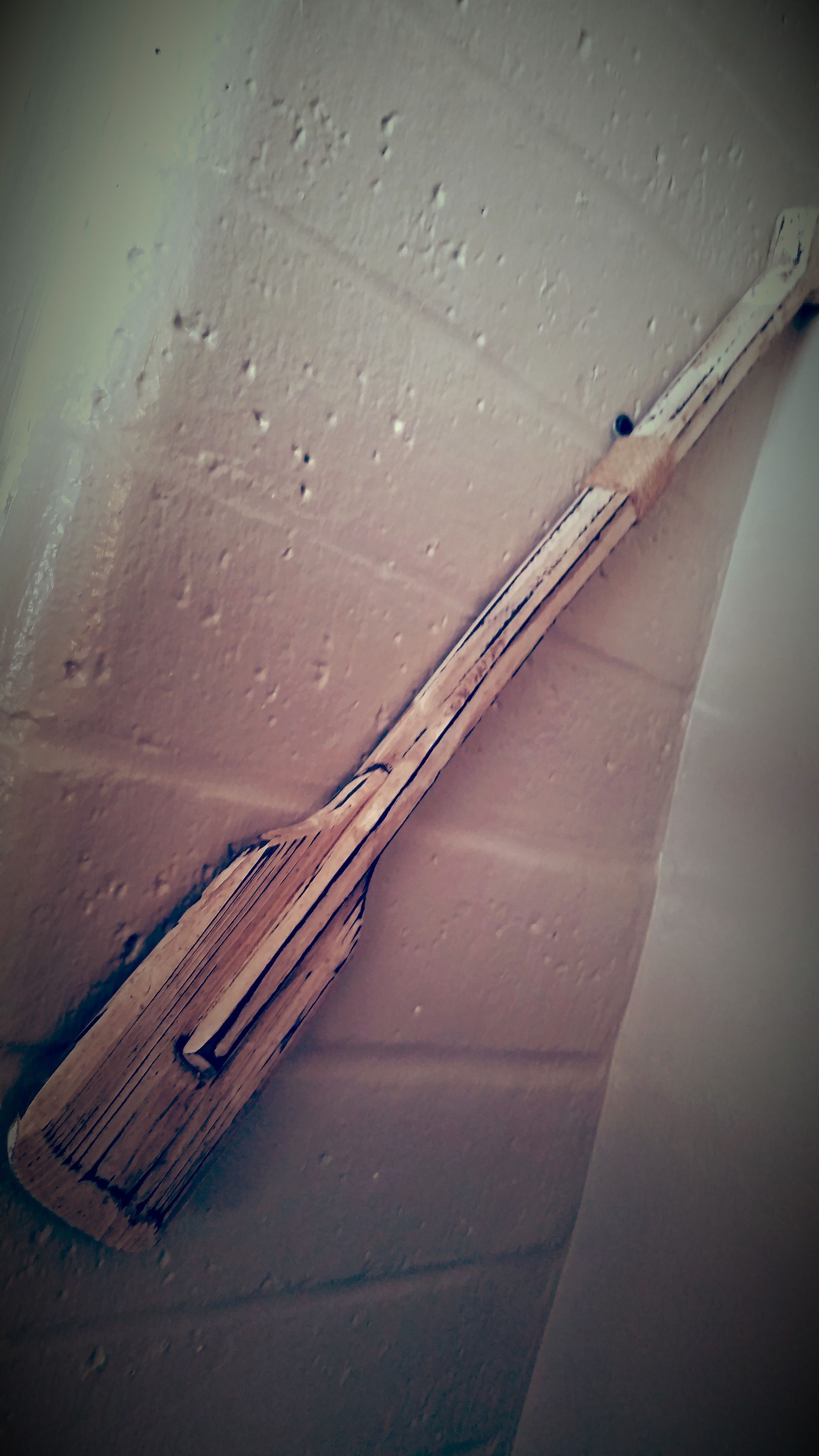 Wooden broom leaning against a white textured wall, lit by soft indoor light.