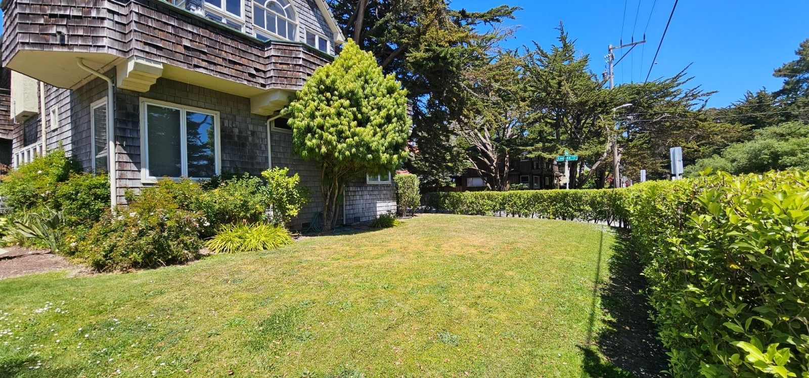 Sunny front yard with green lawn, shrubs, and a house with a balcony and large windows