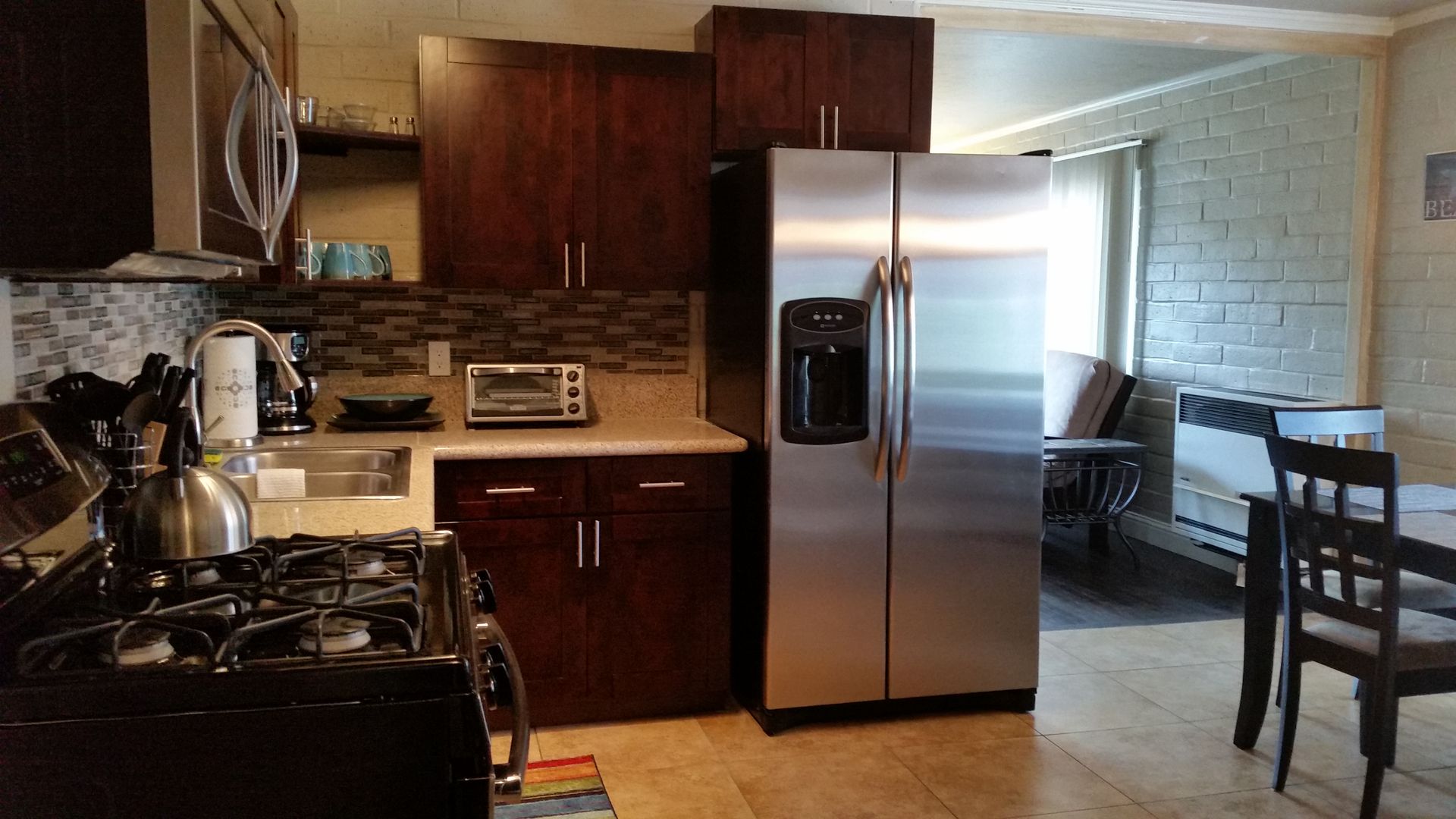 Kitchen with stainless steel fridge, dark wood cabinets, gas stove, and a dining area by a brick wall.