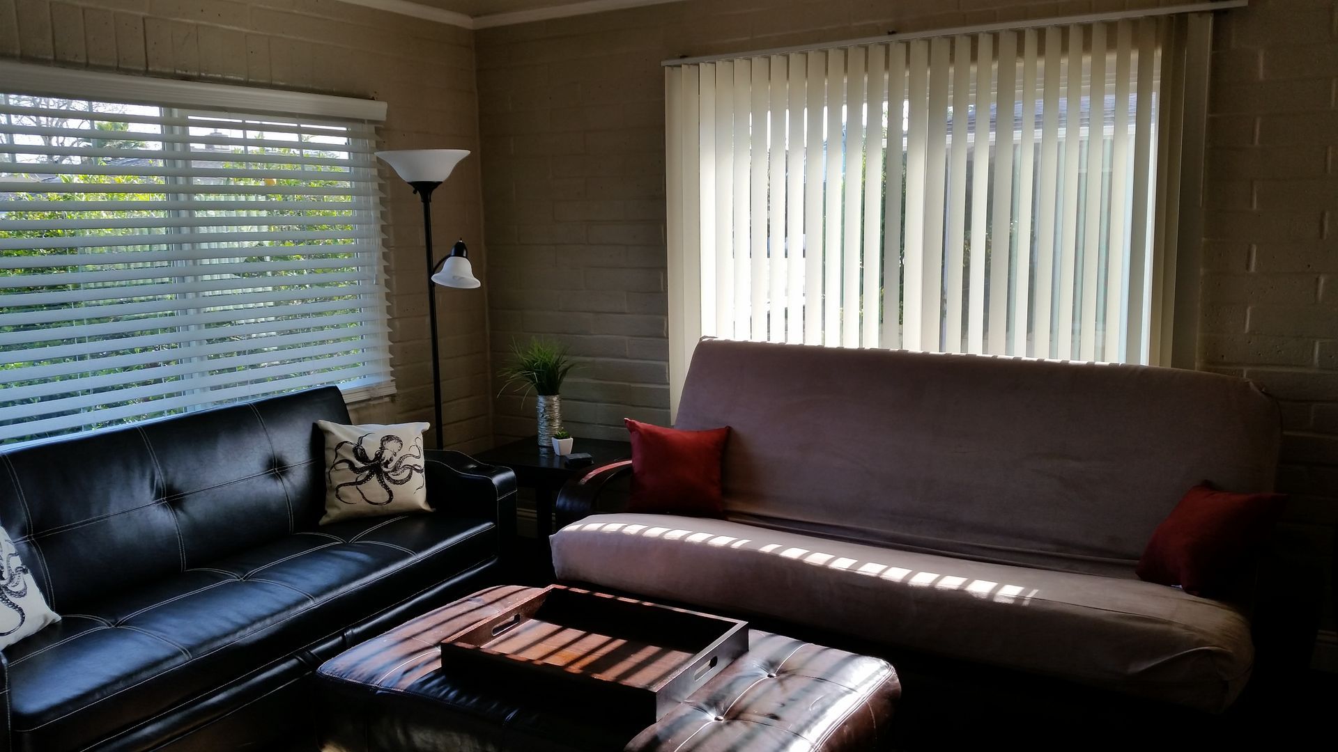 Living room with black sofa, beige chaise, ottoman, and large windows with blinds and curtains
