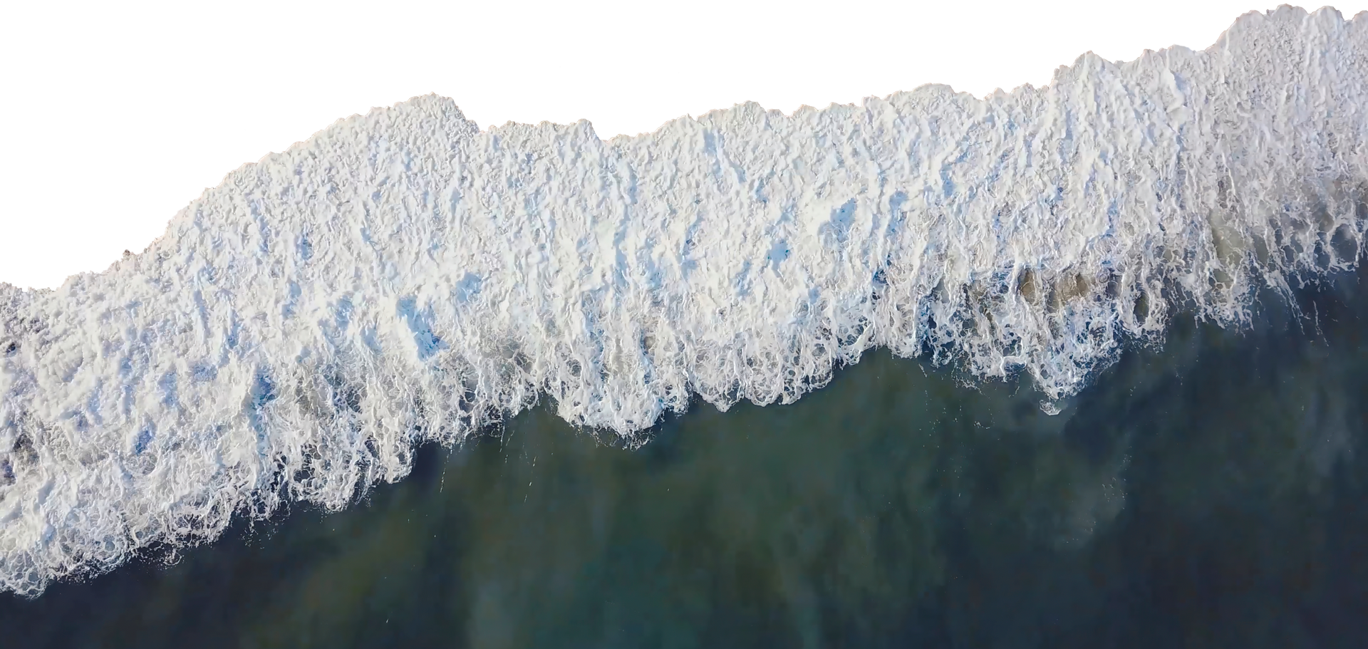 Aerial view of white surf crashing along a dark shoreline