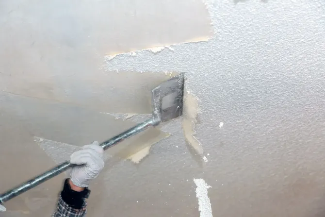 Long-handle scraper removing popcorn texture from drywall.