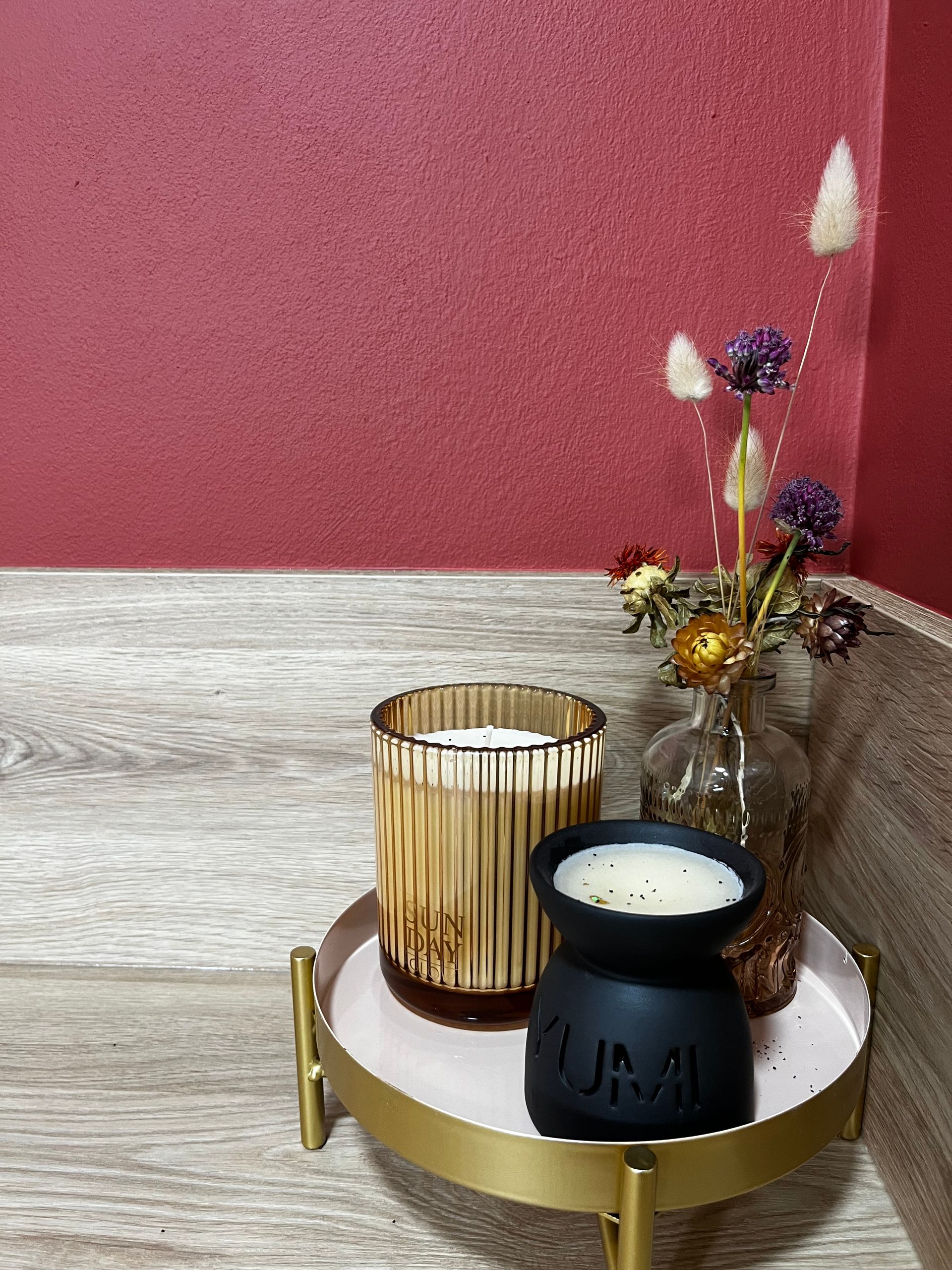 Deux bougies sont posées sur un plateau à côté d'un vase de fleurs séchées.
