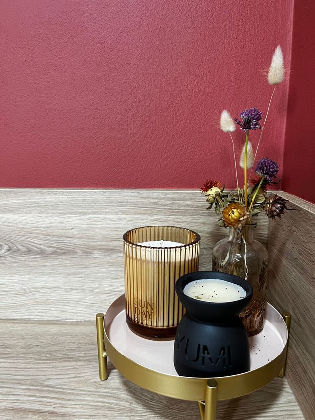 Deux bougies sont posées sur un plateau à côté d'un vase de fleurs séchées.