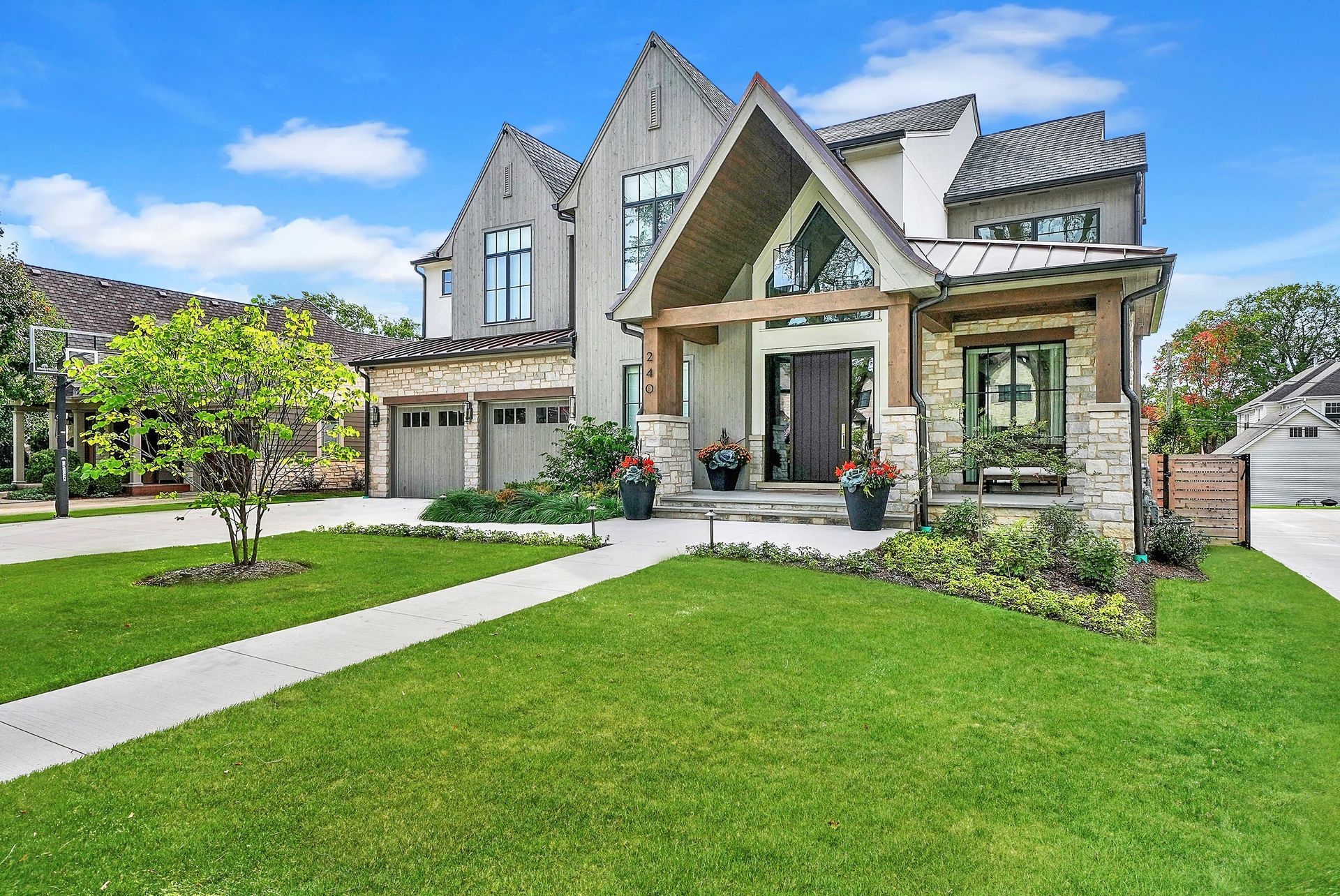 Modern two-story house with stone facade, green lawn, driveway, and landscaped front yard