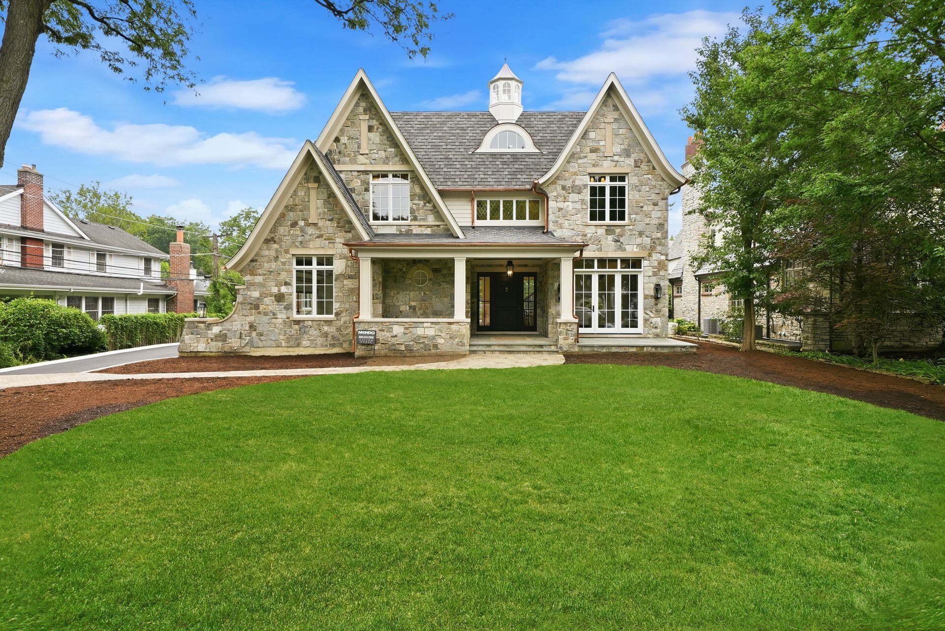 Stone house with a front porch and large green lawn under a blue sky