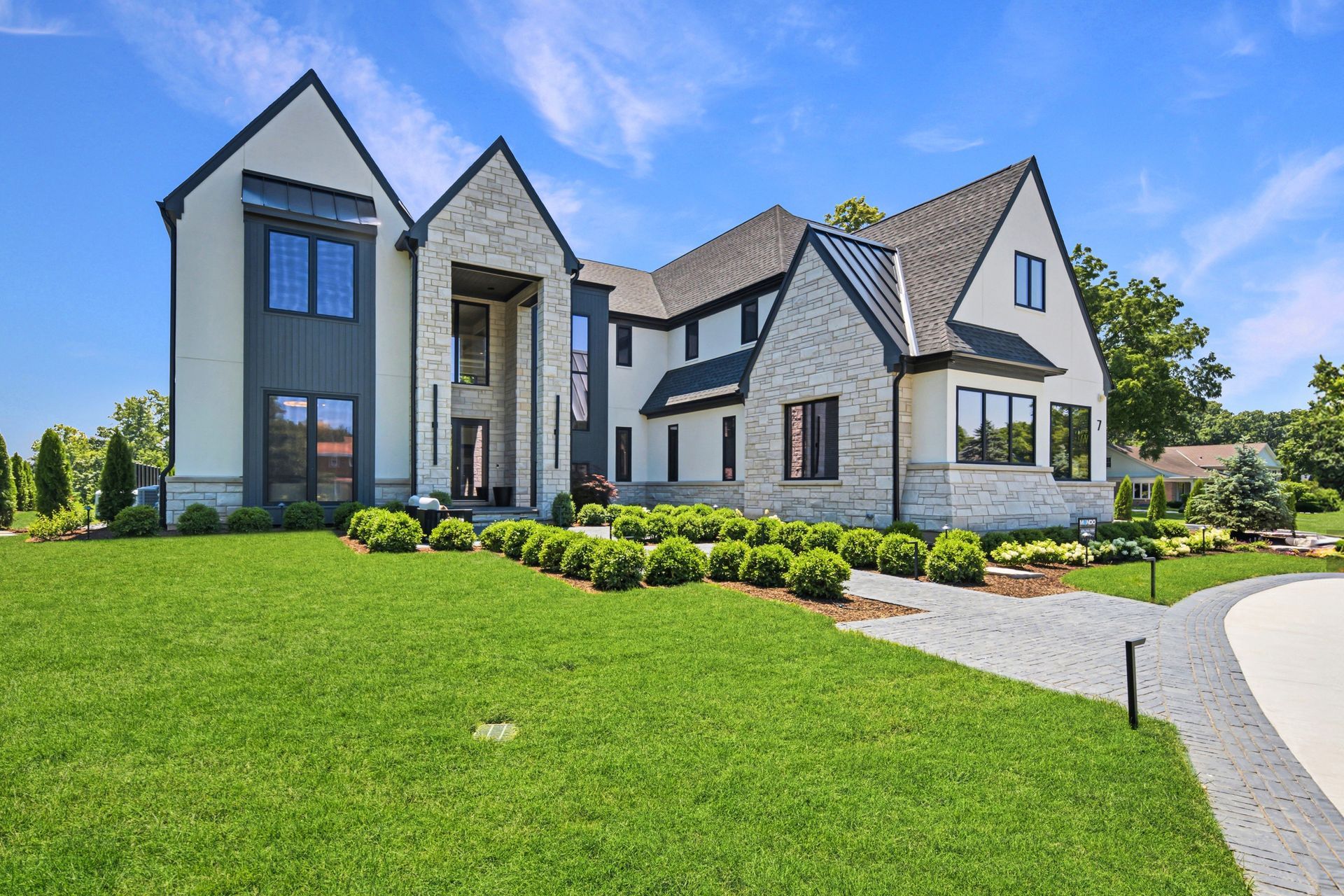 Large modern stone-and-white suburban house with a manicured lawn and curved driveway
