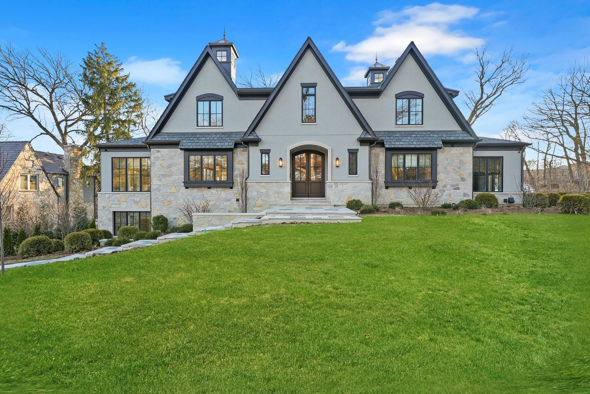 Large gray stone house with steep gables and a manicured green lawn under a clear sky