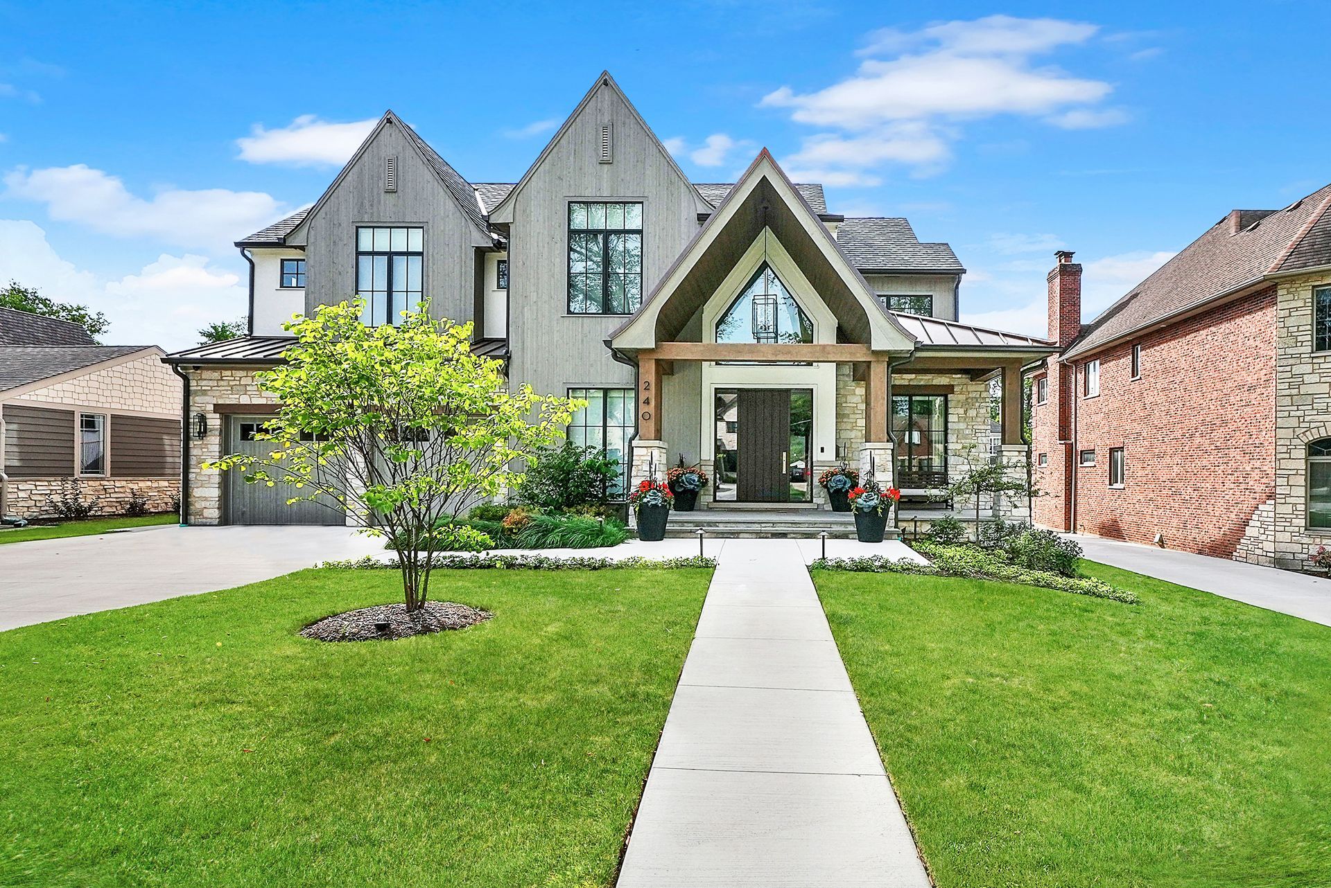 Large gray suburban house with a manicured lawn and a concrete walkway leading to the front entrance