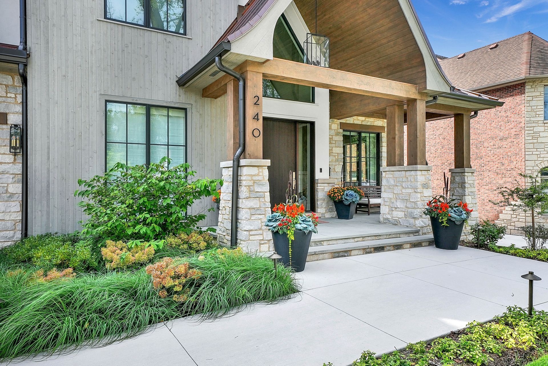 Apartment entrance with covered porch, potted flowers, and a concrete walkway in front of brick and wood siding