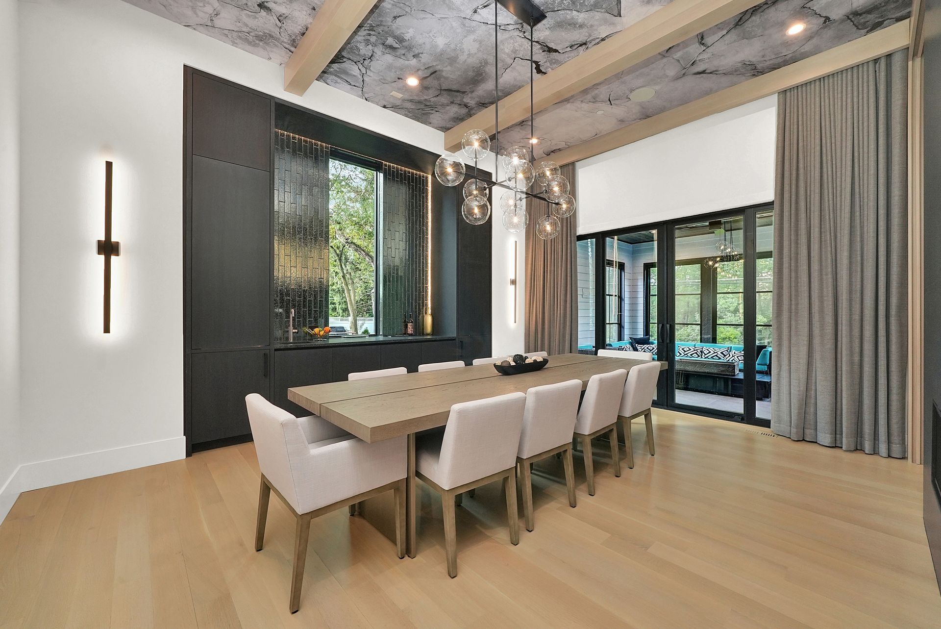 Modern dining room with a long table, upholstered chairs, floor-to-ceiling windows, and curtains