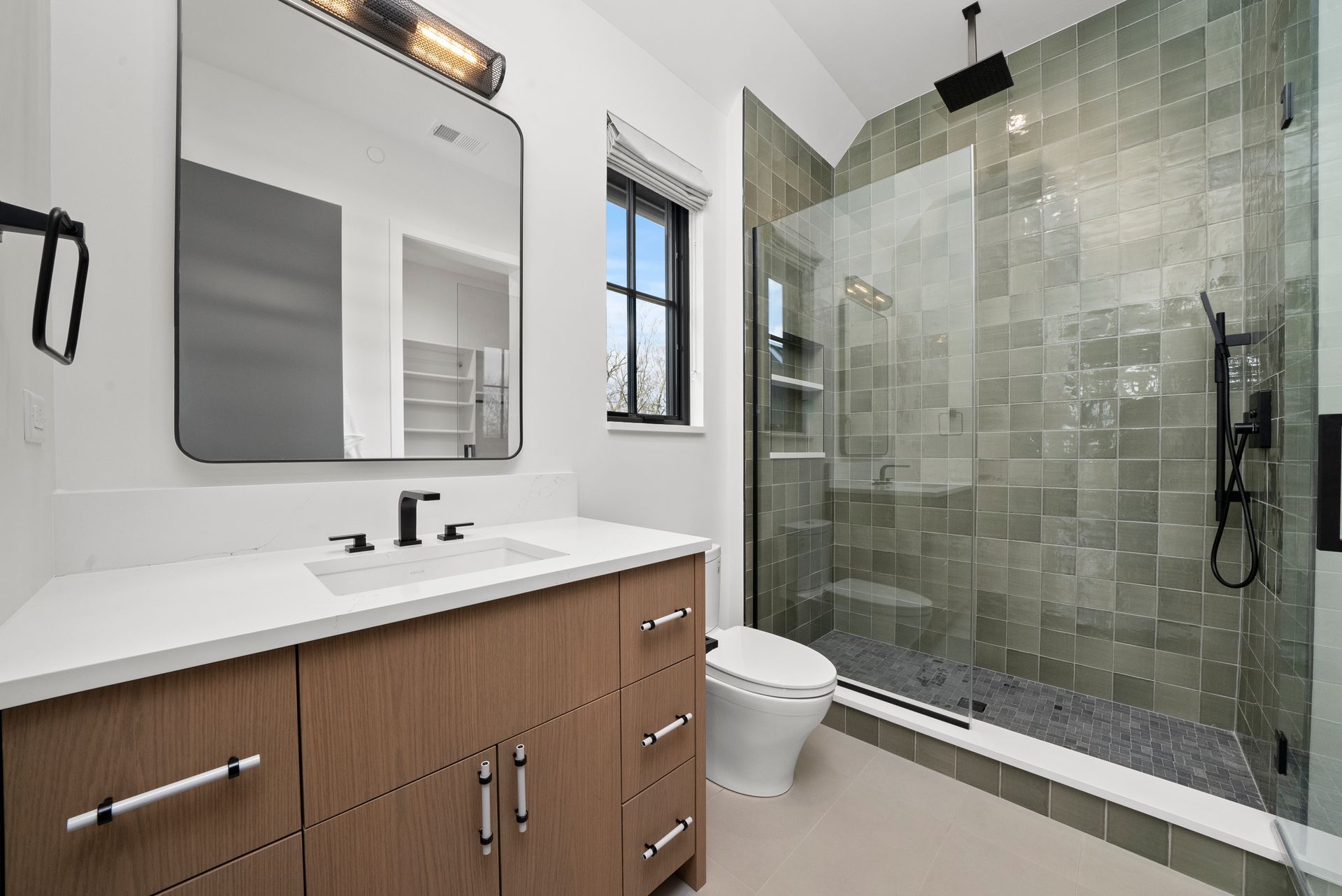 Modern bathroom with wood vanity, large mirror, and glass-enclosed shower with gray tile.