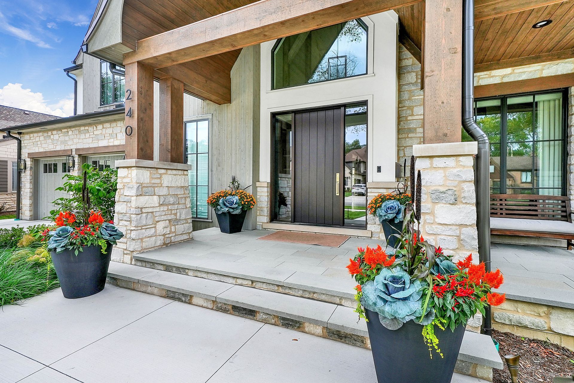 Front porch entrance with stone columns, dark front door, and black planters of red flowers