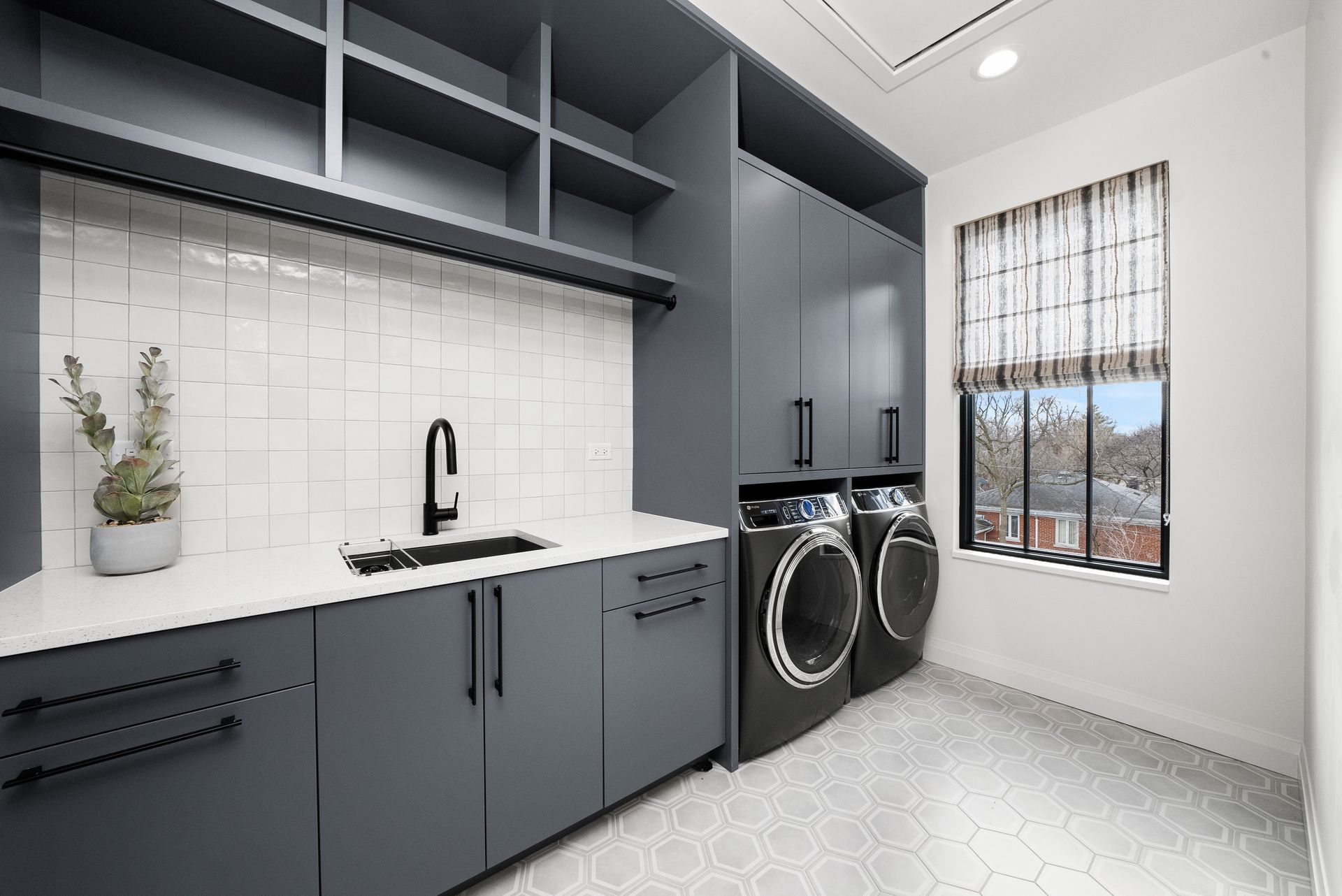 Modern laundry room with gray cabinets, white tile, washer-dryer, and a window with mountain view