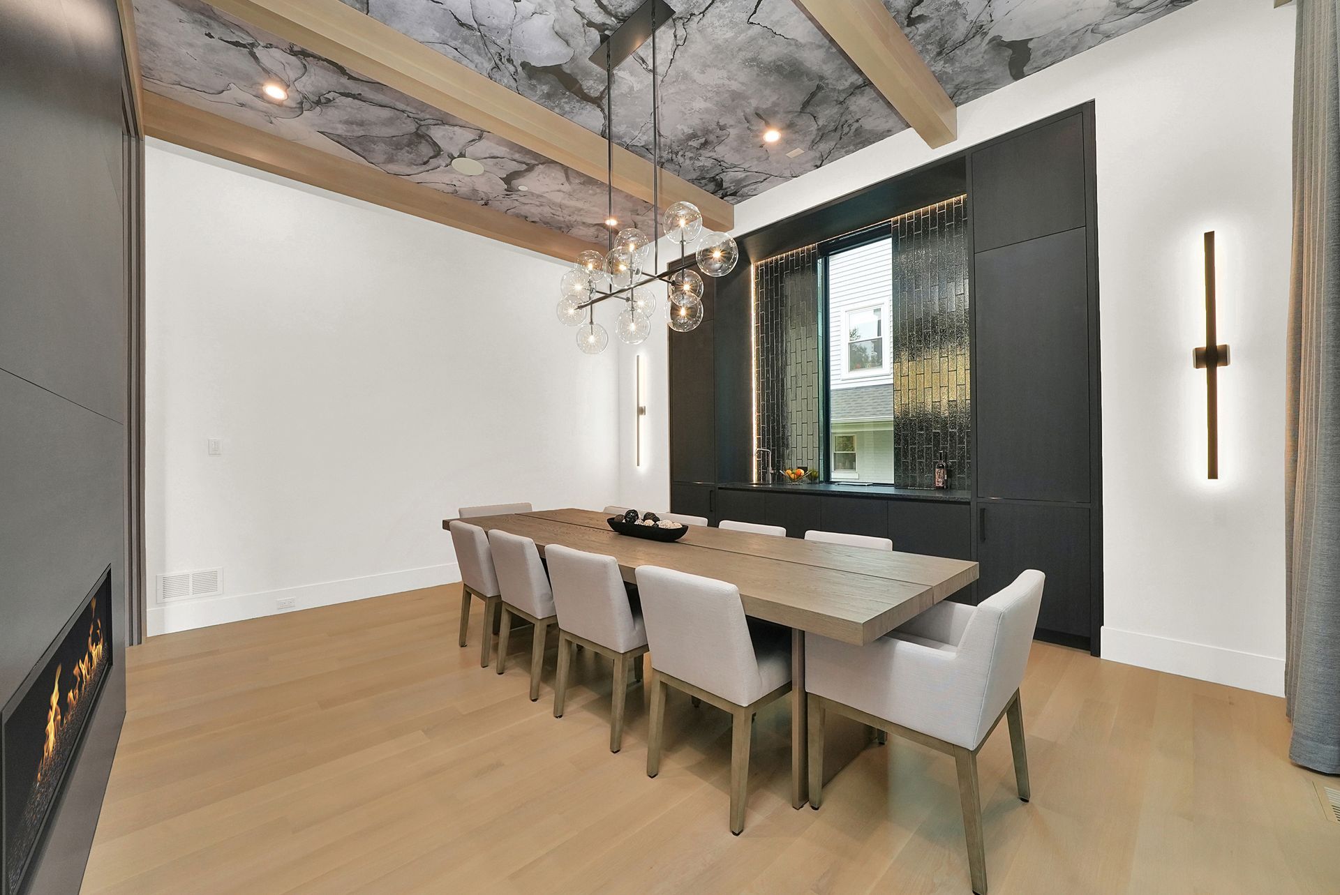 Modern dining room with long table, beige chairs, chandelier, and black accent wall