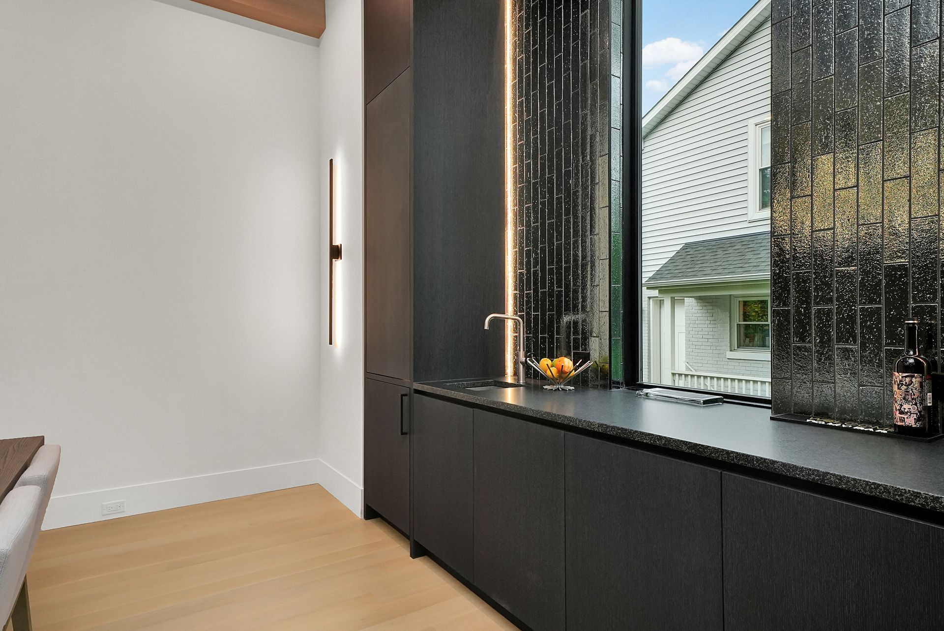 Modern room with light wood floor, black cabinetry, and large window overlooking a house