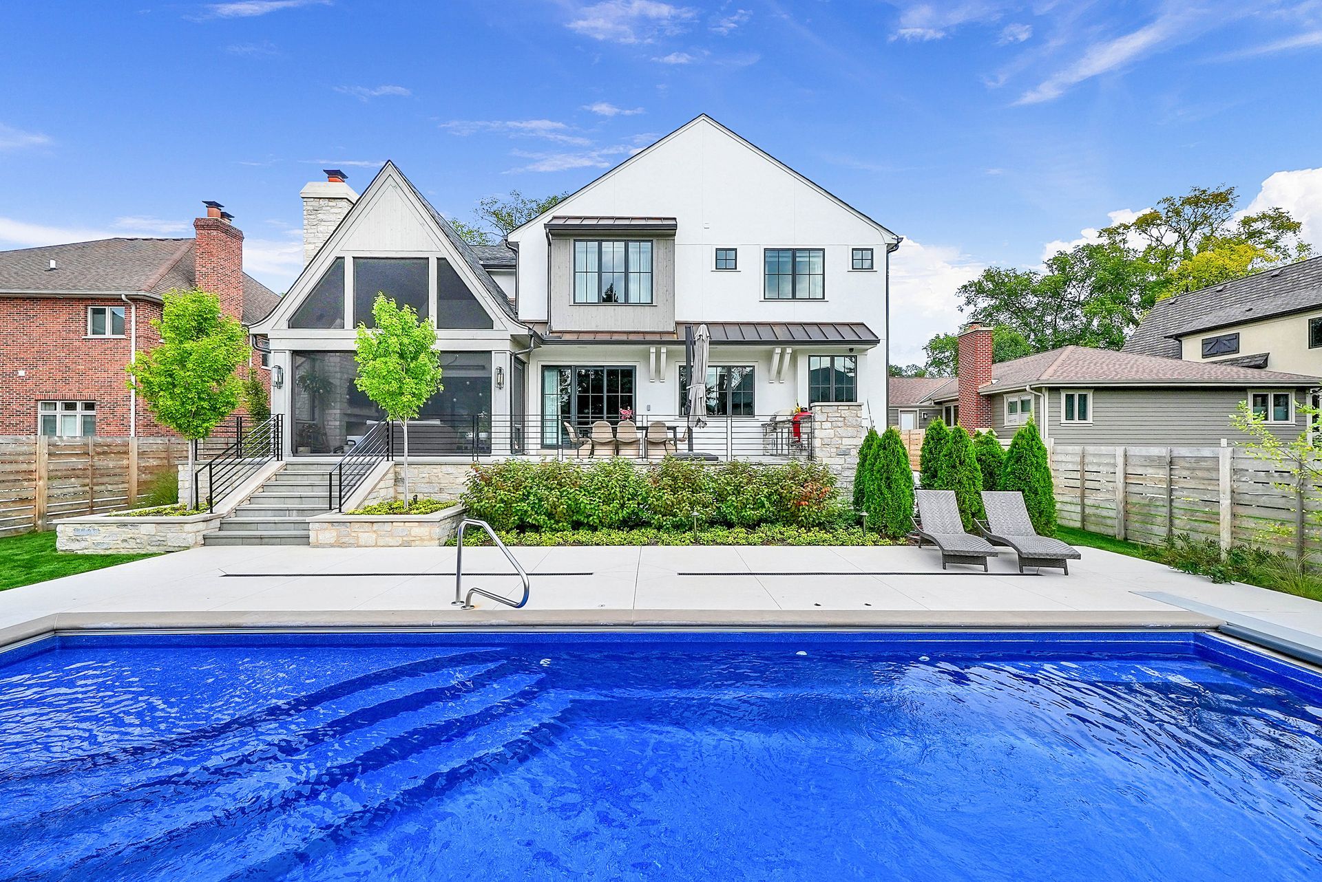 White house with a pool in the foreground and a landscaped backyard, seen on a sunny day