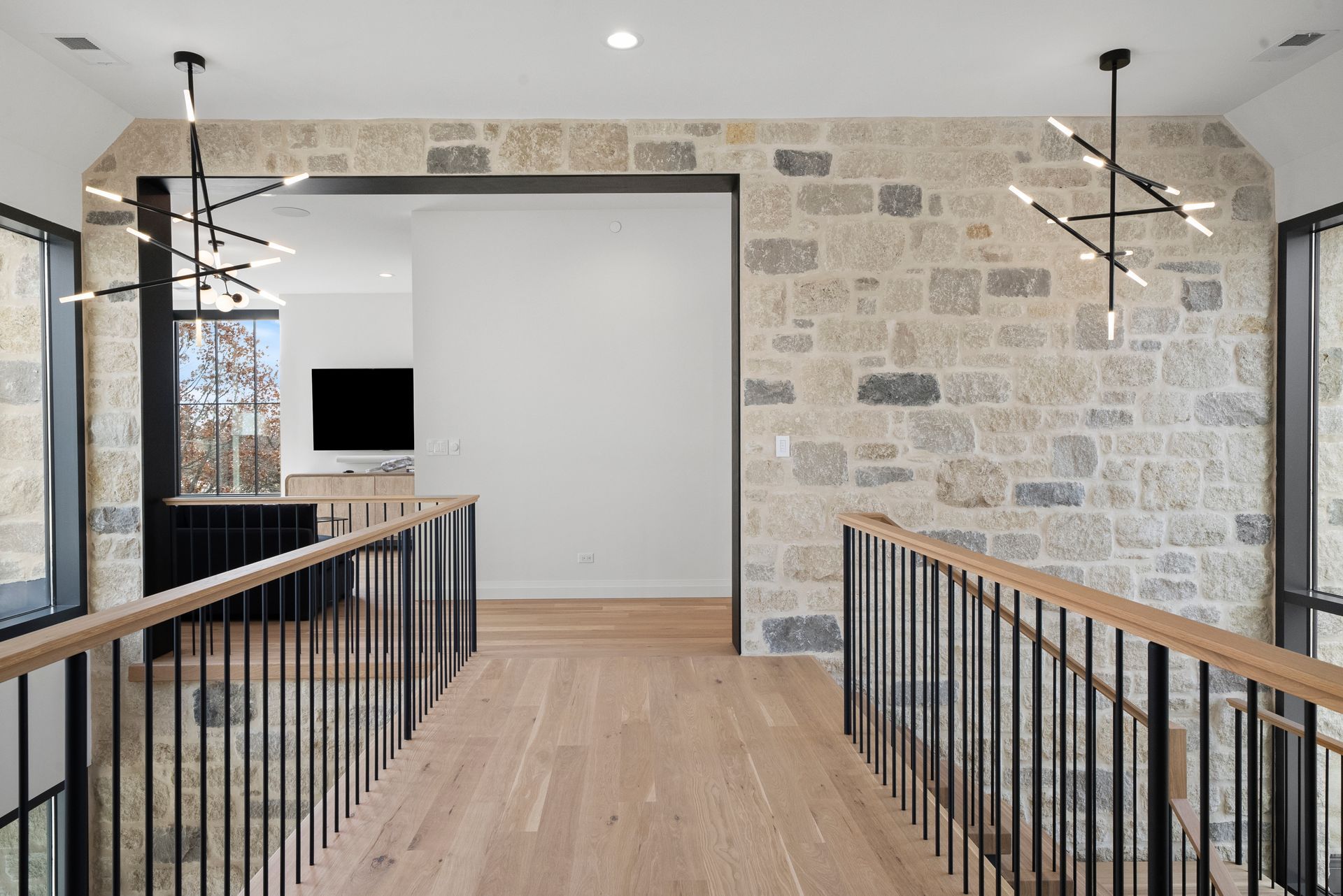 Modern interior hallway with wood floors, black railings, stone wall, and pendant lights