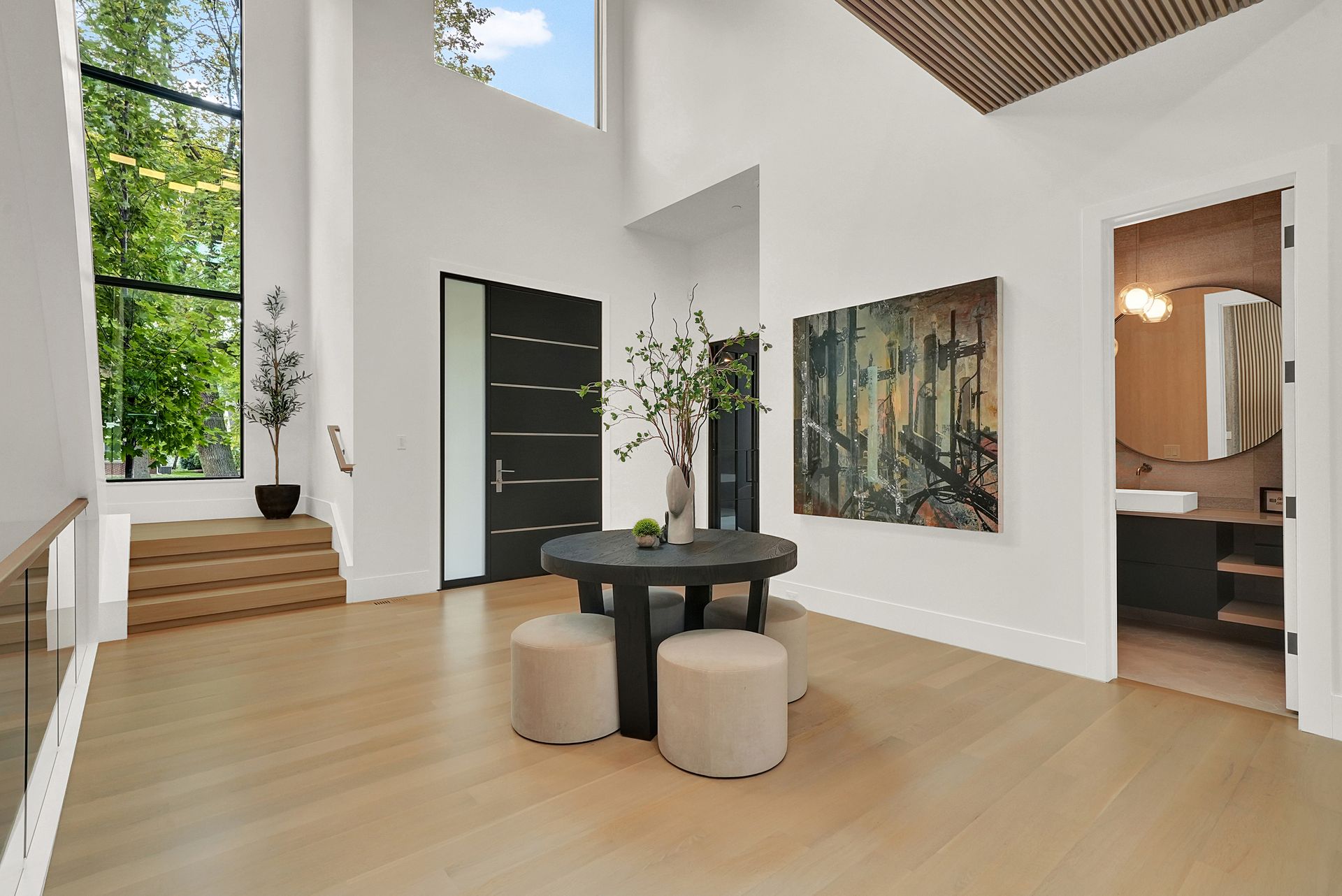 Bright modern foyer with staircase, black front door, round table, and large wall art