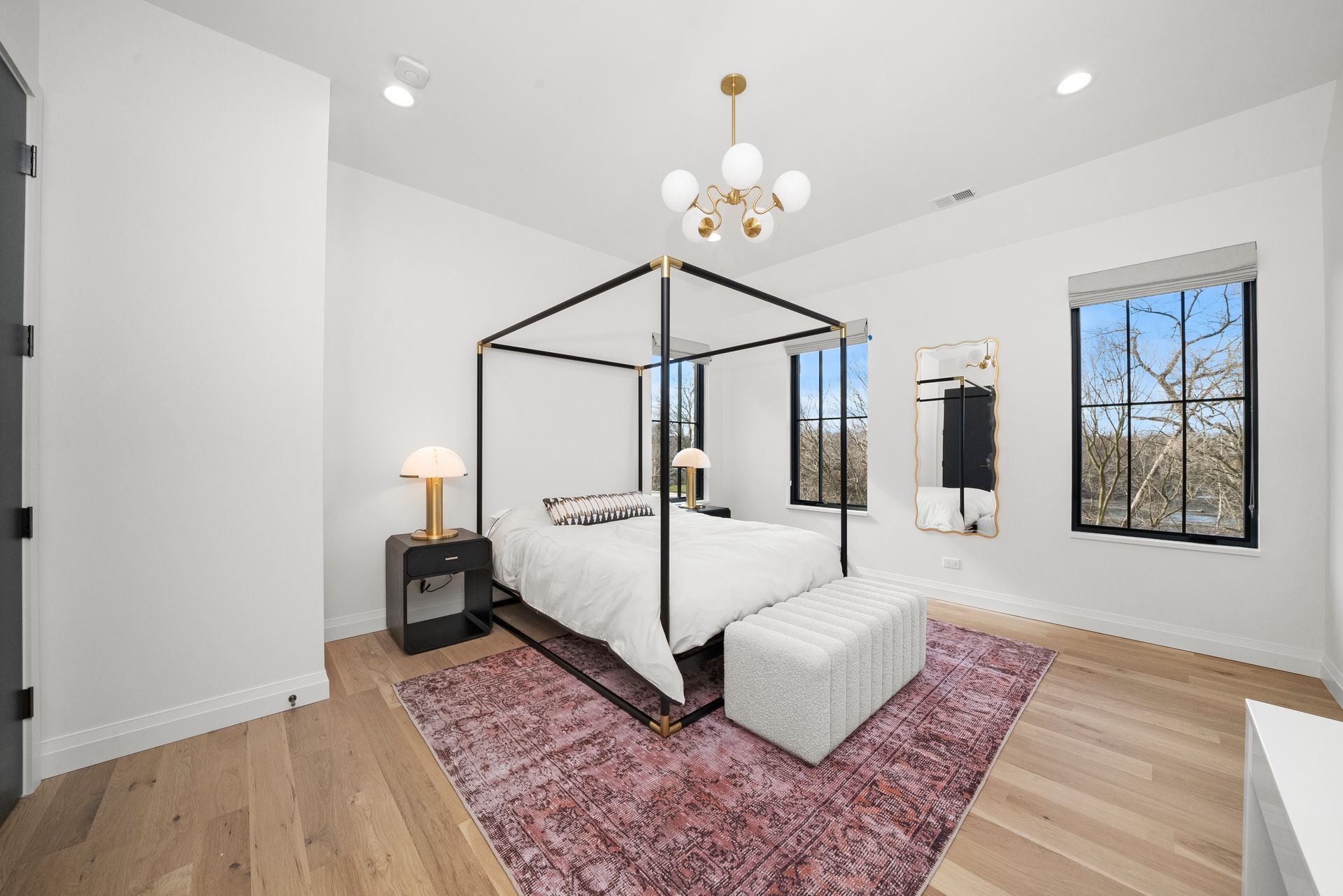 Bright modern bedroom with a black four-poster bed, pink rug, and large windows